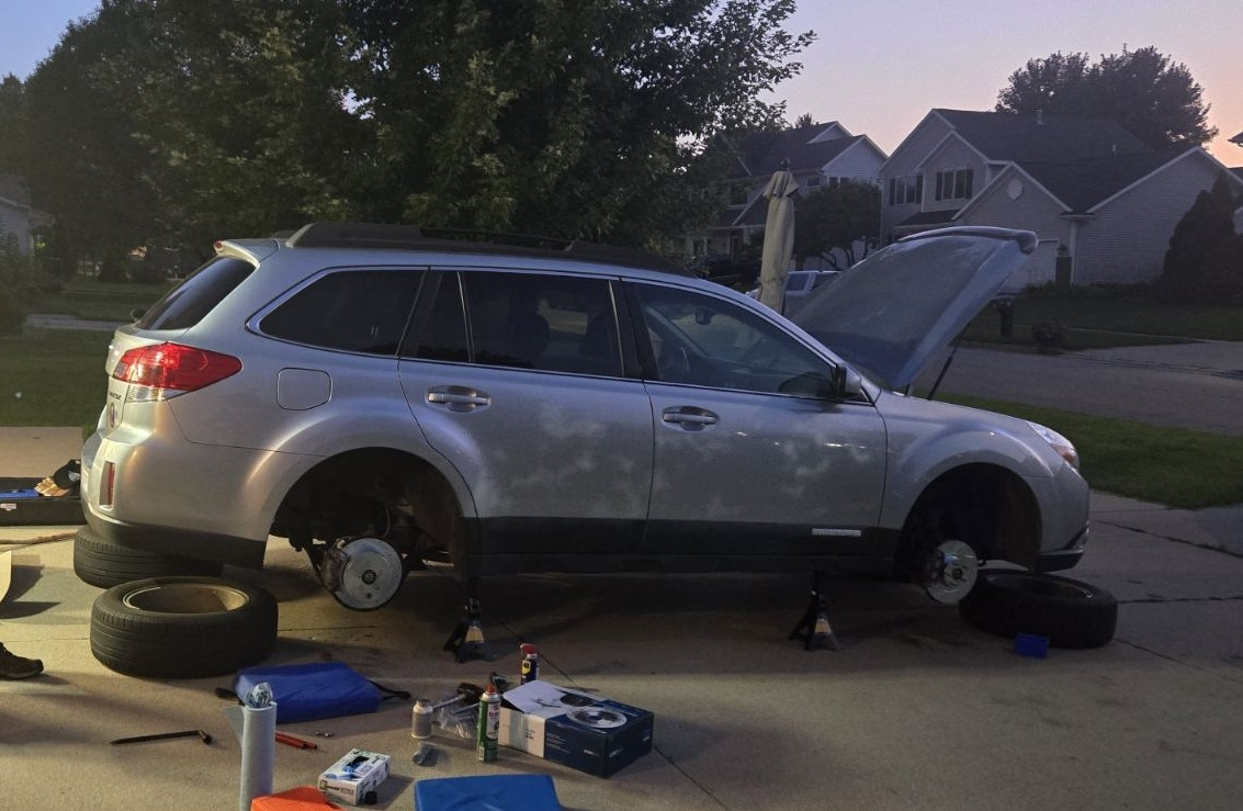 Silver Subaru Outback up on Jack stands, with all the wheels removed. Shiny new rotors have been installed