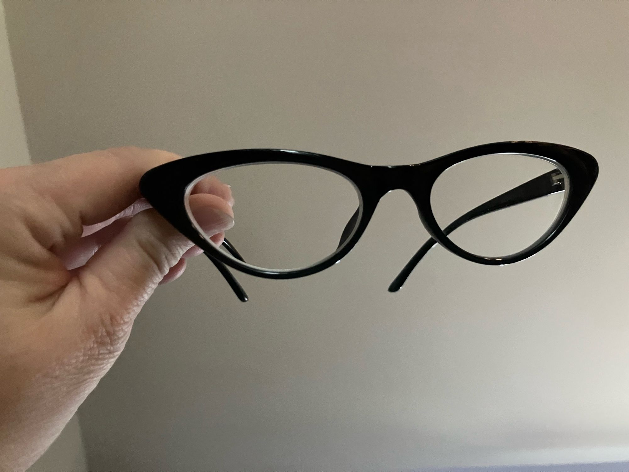 A hand holding up a pair of extremely cat eye glasses with black frames