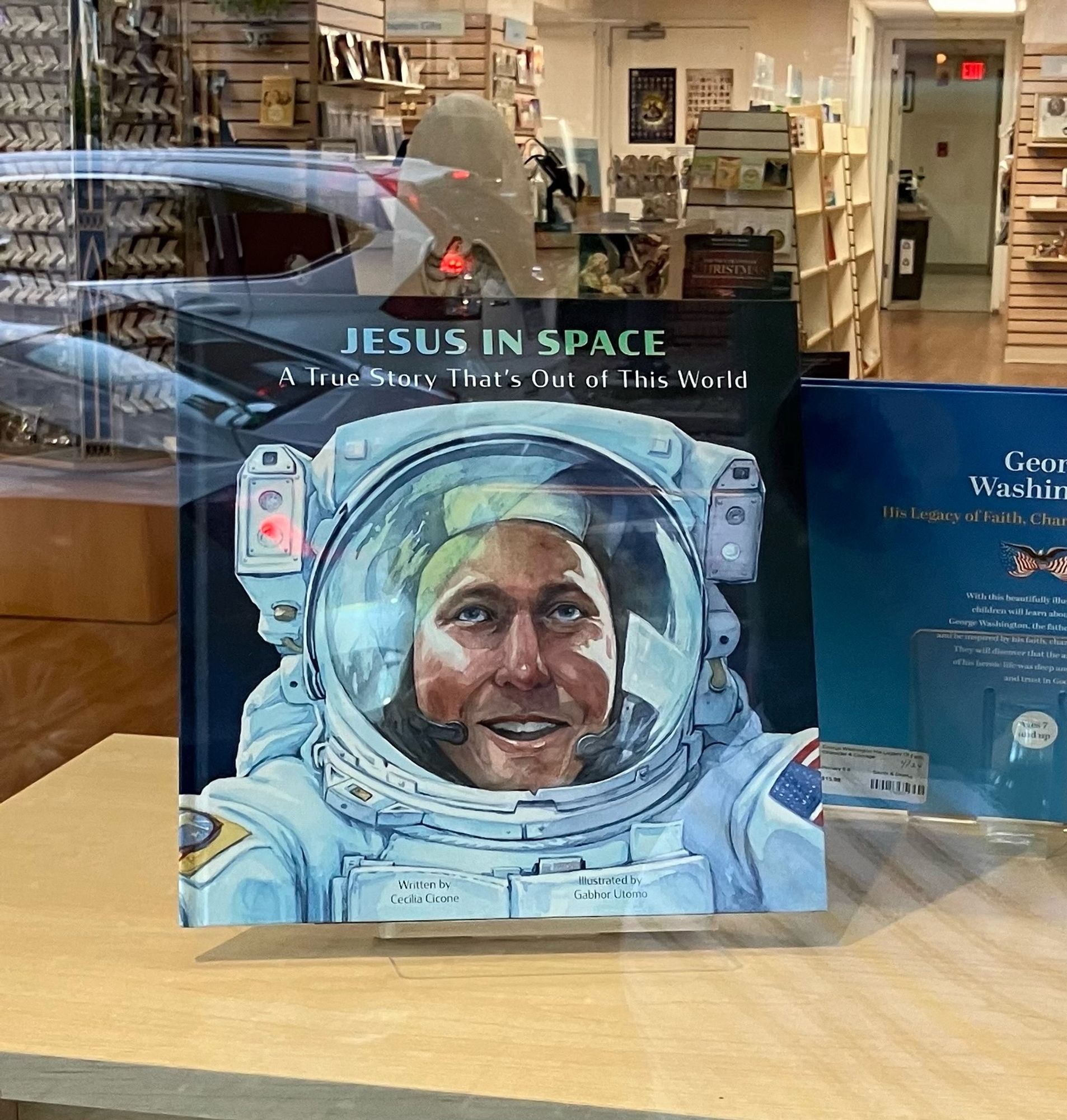 A kid’s book in the window of the nun bookstore in Old Town with a watercolor picture of an astronaut and the title “Jesus In Space”