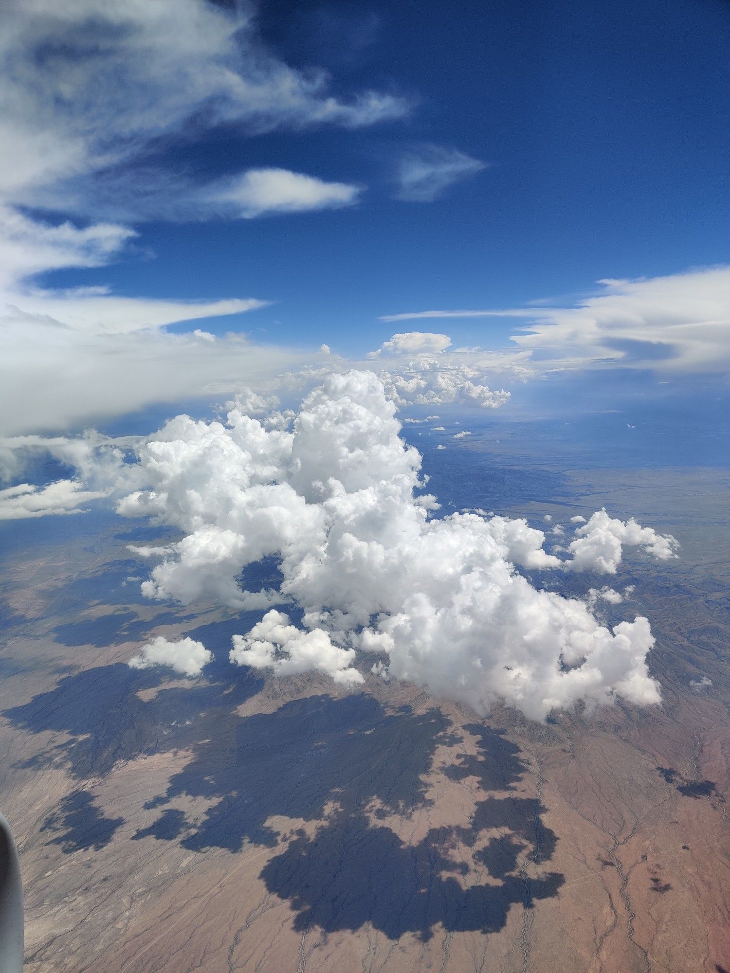 A cloud casting a shadow on the ground from the perspective of an airplane window