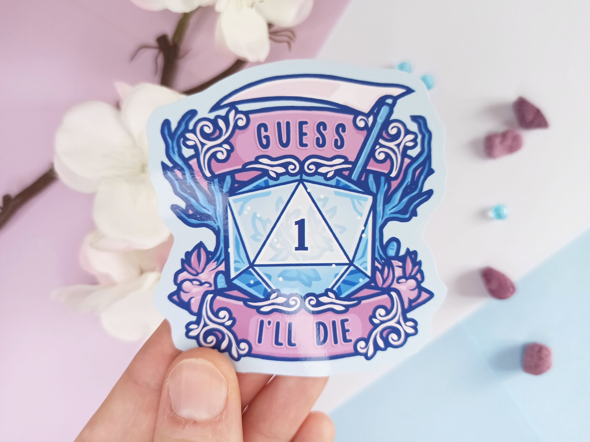 Hand holding up a sticker with the design of a DnD dice that rolled "1", and text "Guess I'll die" framing it.