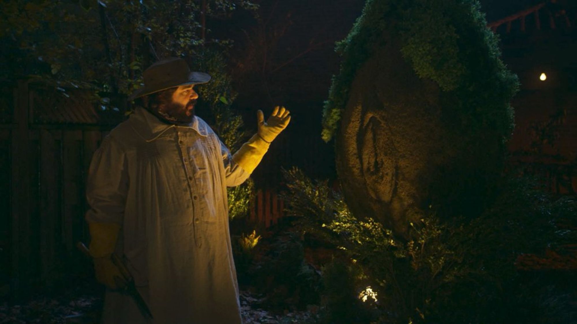 still image from the TV show What We Do In The Shadows. Lazslo, played by Matt Berry, stands in front of a topiary cut to very obviously resemble a vulva.