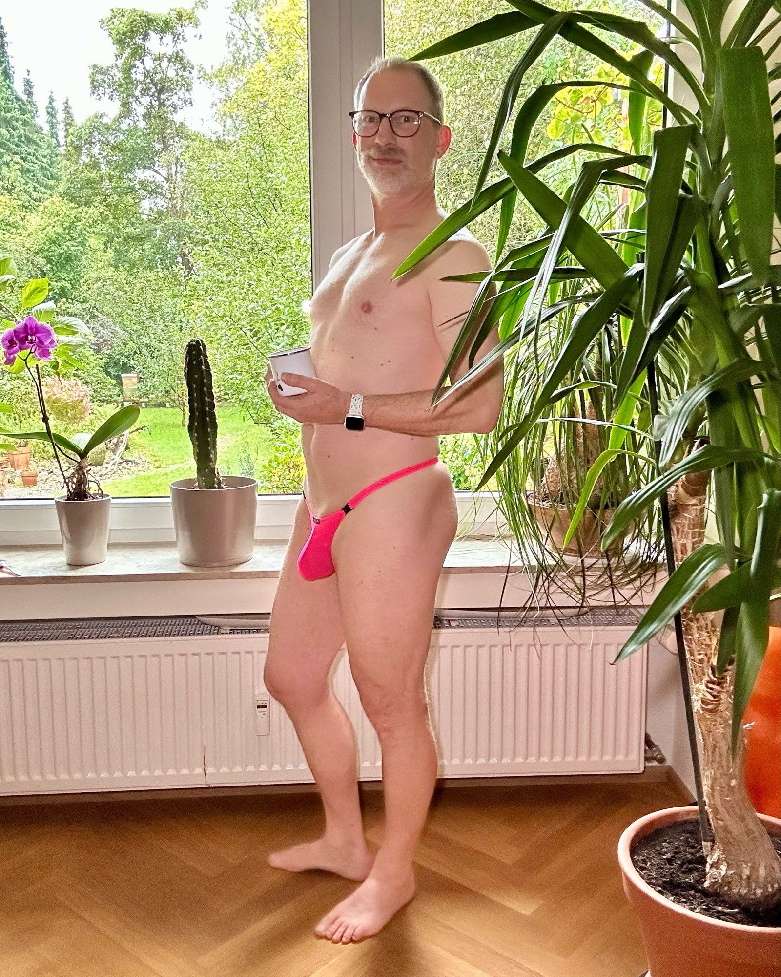 Standing in front of a window in the living room wearing only a pink Wojoer thong with clips. Turned around towards the camera to show my bulge, holding a cup of coffee in my hands