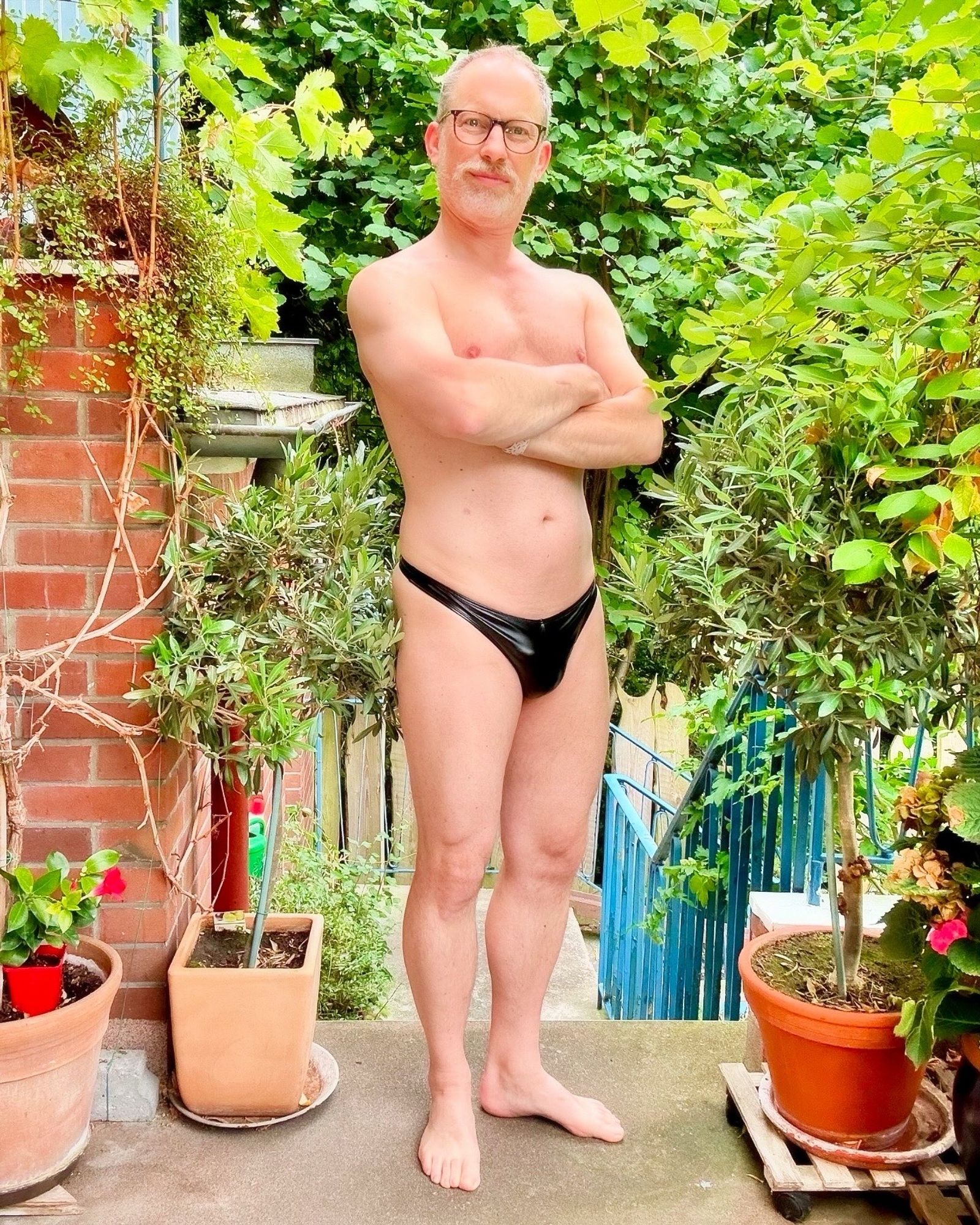 On the deck, front view of me, wearing a black vegan Omohonia leather thong, arms crossed at chest height