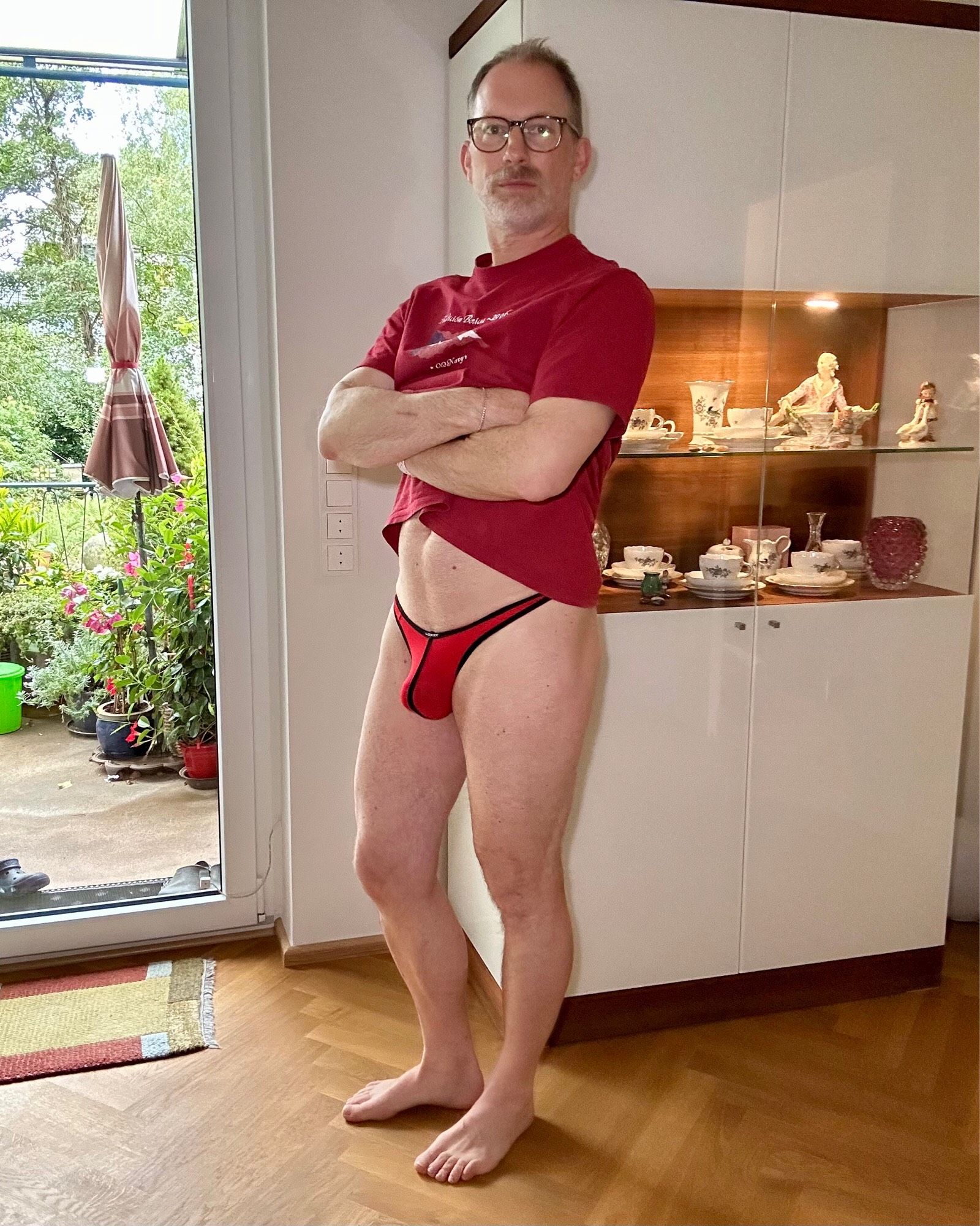 Facing the camera wearing a red Wojoer thong and a matching tee. Shirt is slid up to display my bulge. Face not looking happy