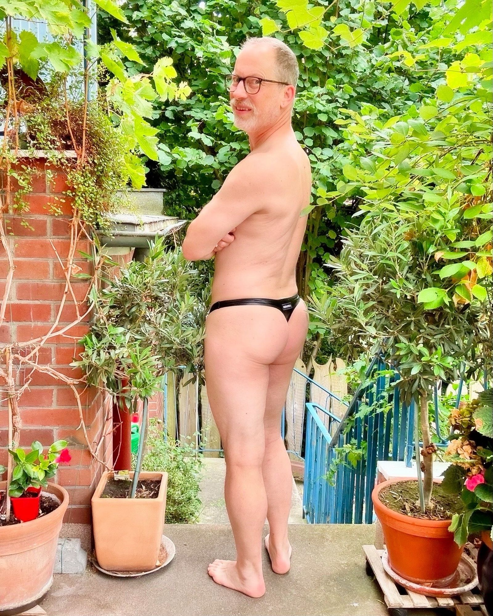 Backside of me in a black vegan Omohonia leather thong, head turned backwards to look into the camera