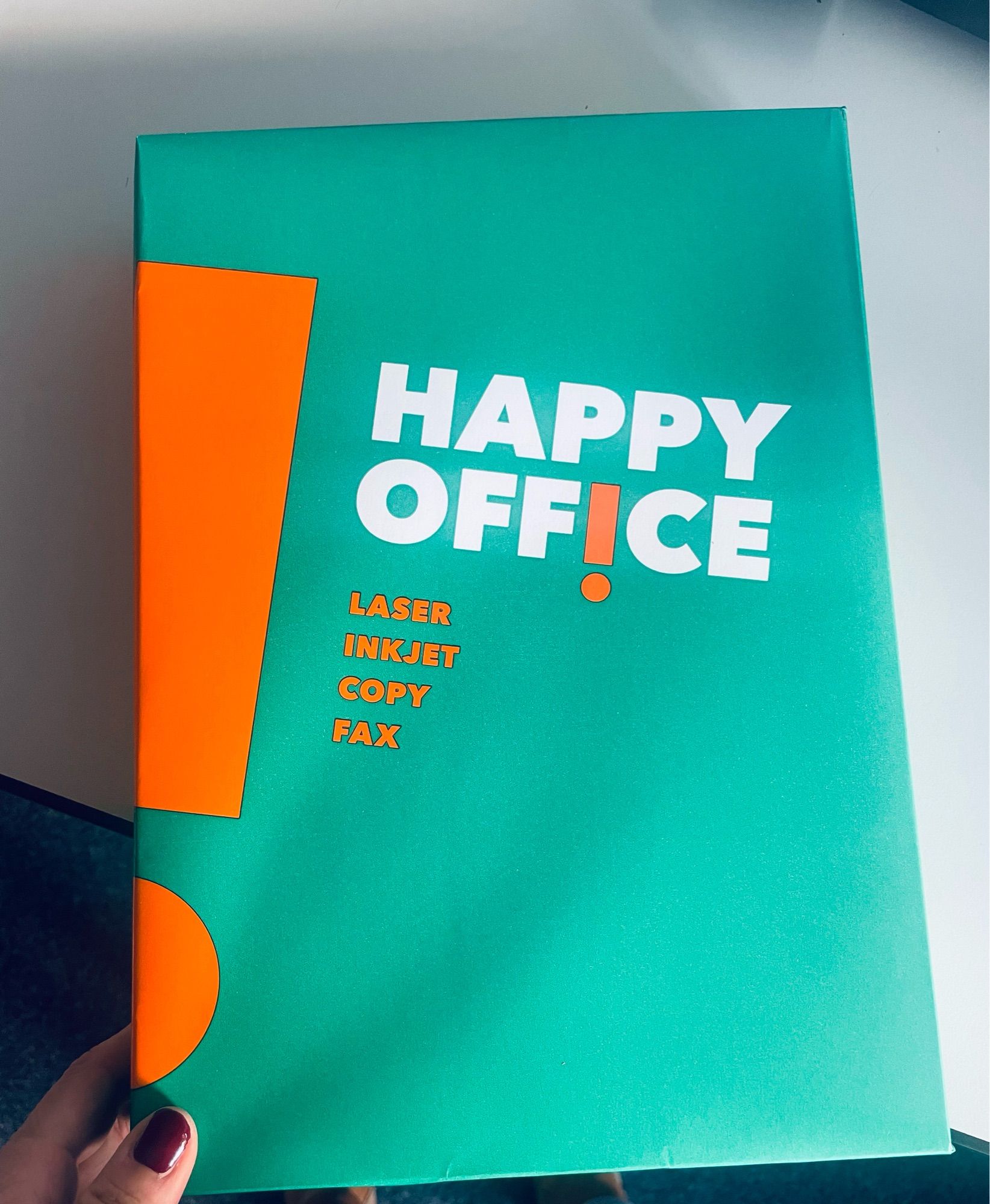 Grün-orangefarbenes Paket mit Kopierpapier mit der weißen Schrift „Happy Office“