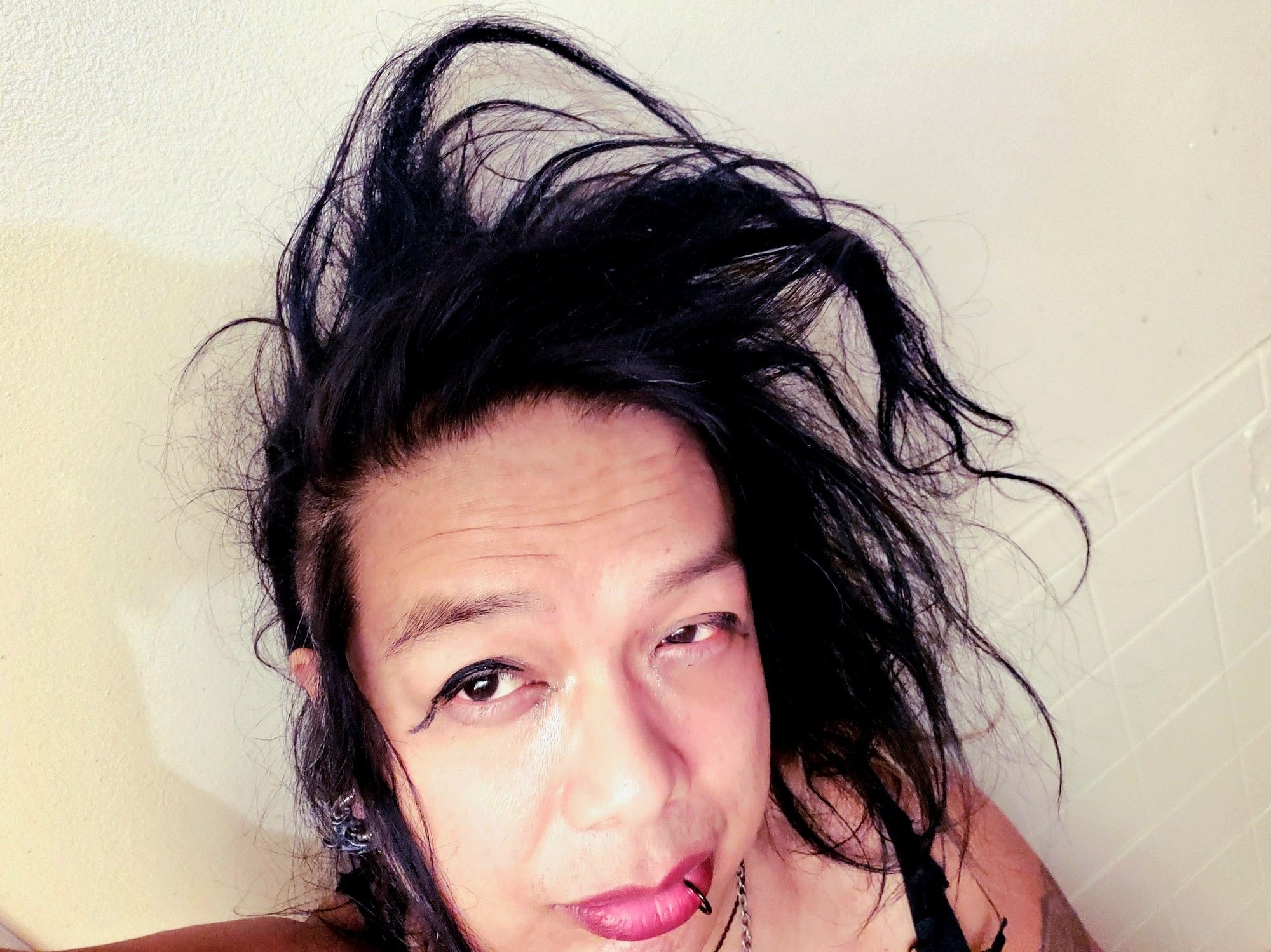 Kei downward angle selfie at wakeup, all face and left shoulder, showing hair sticking up and swooping to Her left, left eye slightly squinted and yesterdays makeup still half on.