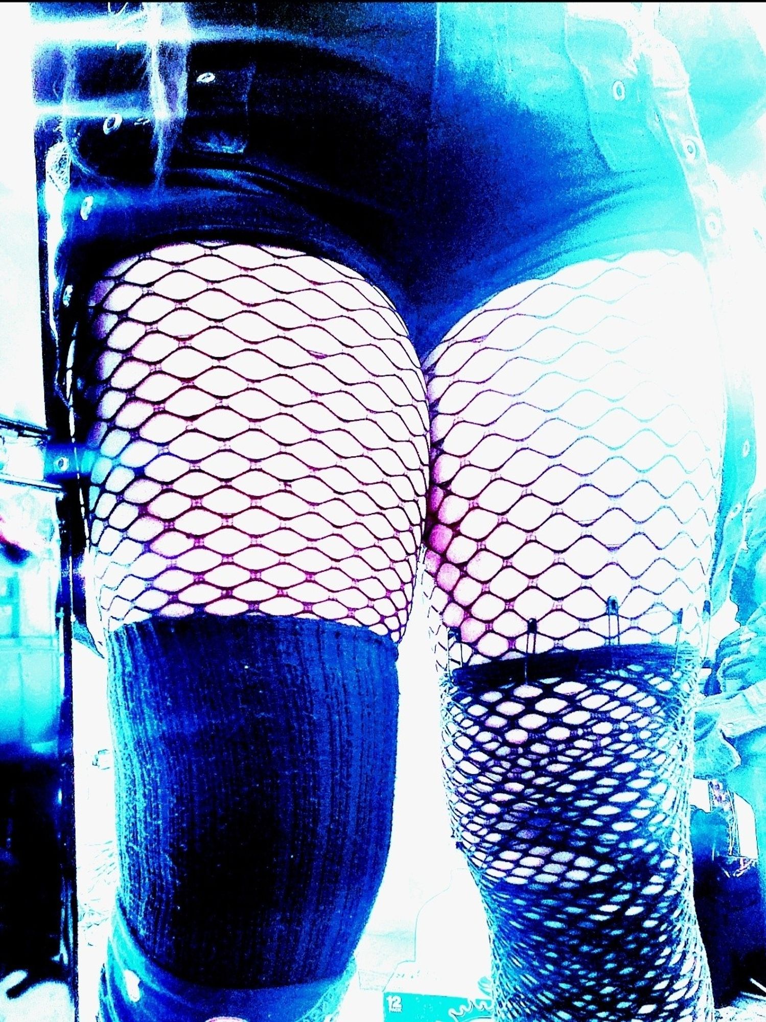 Kei from shins to waist with black knit OverKneeSox on right leg and double layer fishnet on left leg held up with black safety pins, both over fishnet tights with tight black shirts with grommet strap chain hard kightbfromnrightbofnframe and blue LED, contrast boosted and color reduced except for blue, light balance cranked.