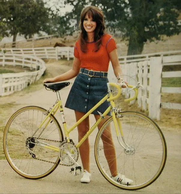 1973 Schwinn Paramount catalog shot, of a young woman standing behind a Paramount step-thru bicycle. 