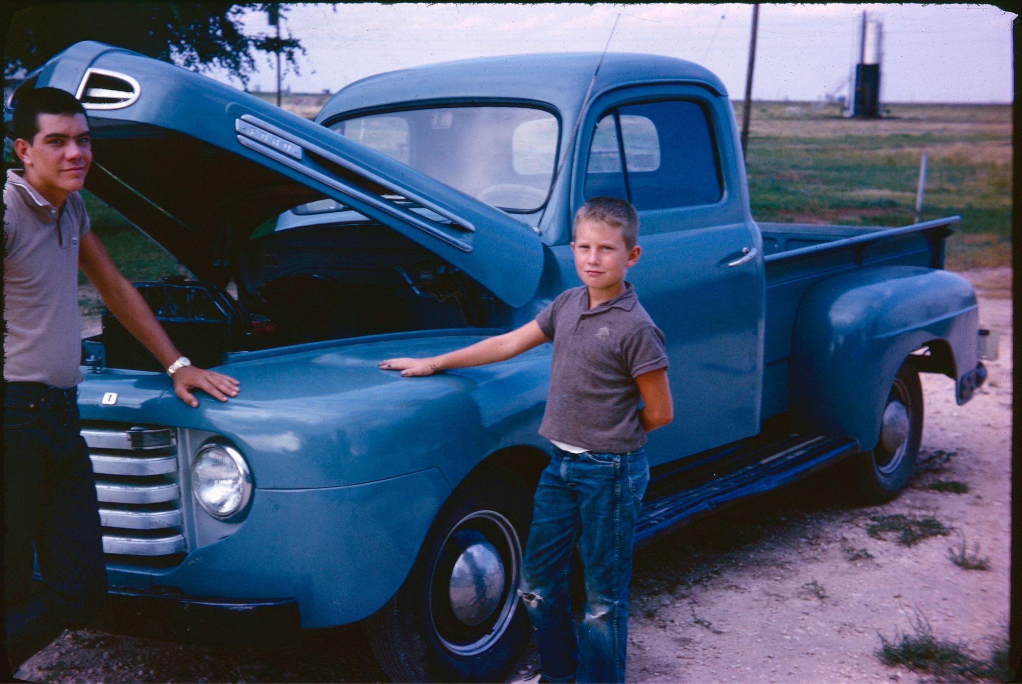 A vintage slide of a 1950s blue Ford truck with two young men standing with pride and putting their hands on it protectively.