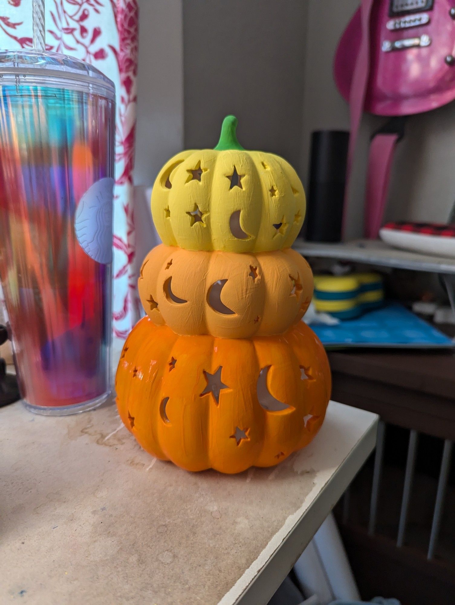 The same ceramic statue of three pumpkins stacked on top of each other, of descending size and with star and moon shaped cutouts. painted yellow, light orange, and orange