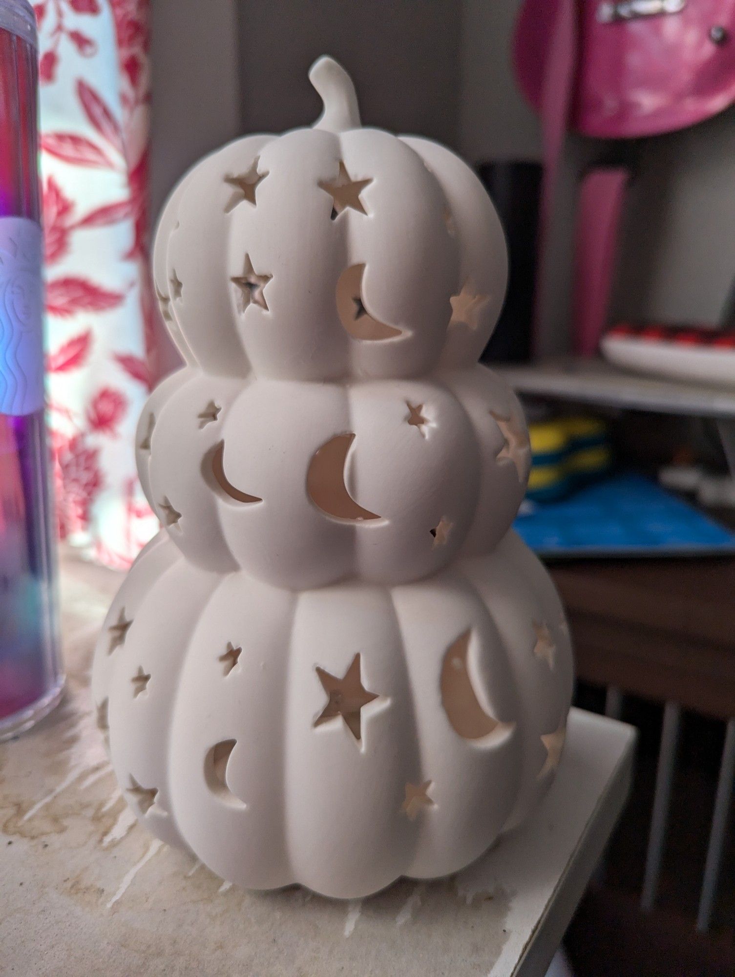 A white ceramic statue of three pumpkins stacked on top of each other, of descending size, with star and moon shaped cutouts.