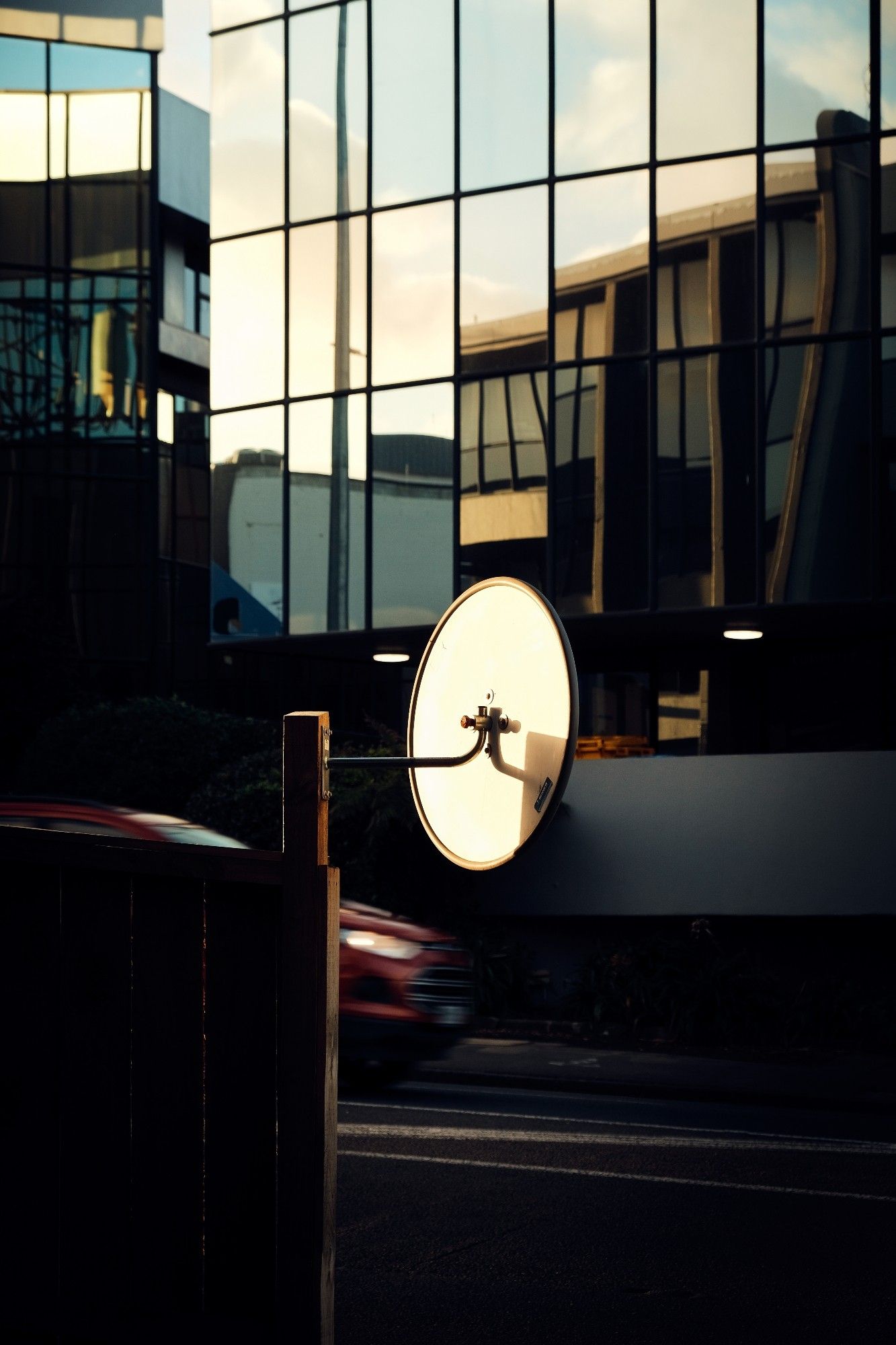 Street photography: composition with glassed buildings, street , a car and road mirror at golden hour light time.