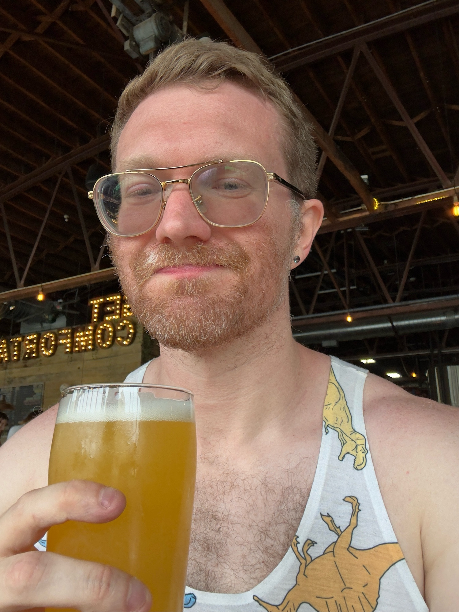 It’s a photo of me drinking a celebratory Pride beer in a rainbow dino tanktop