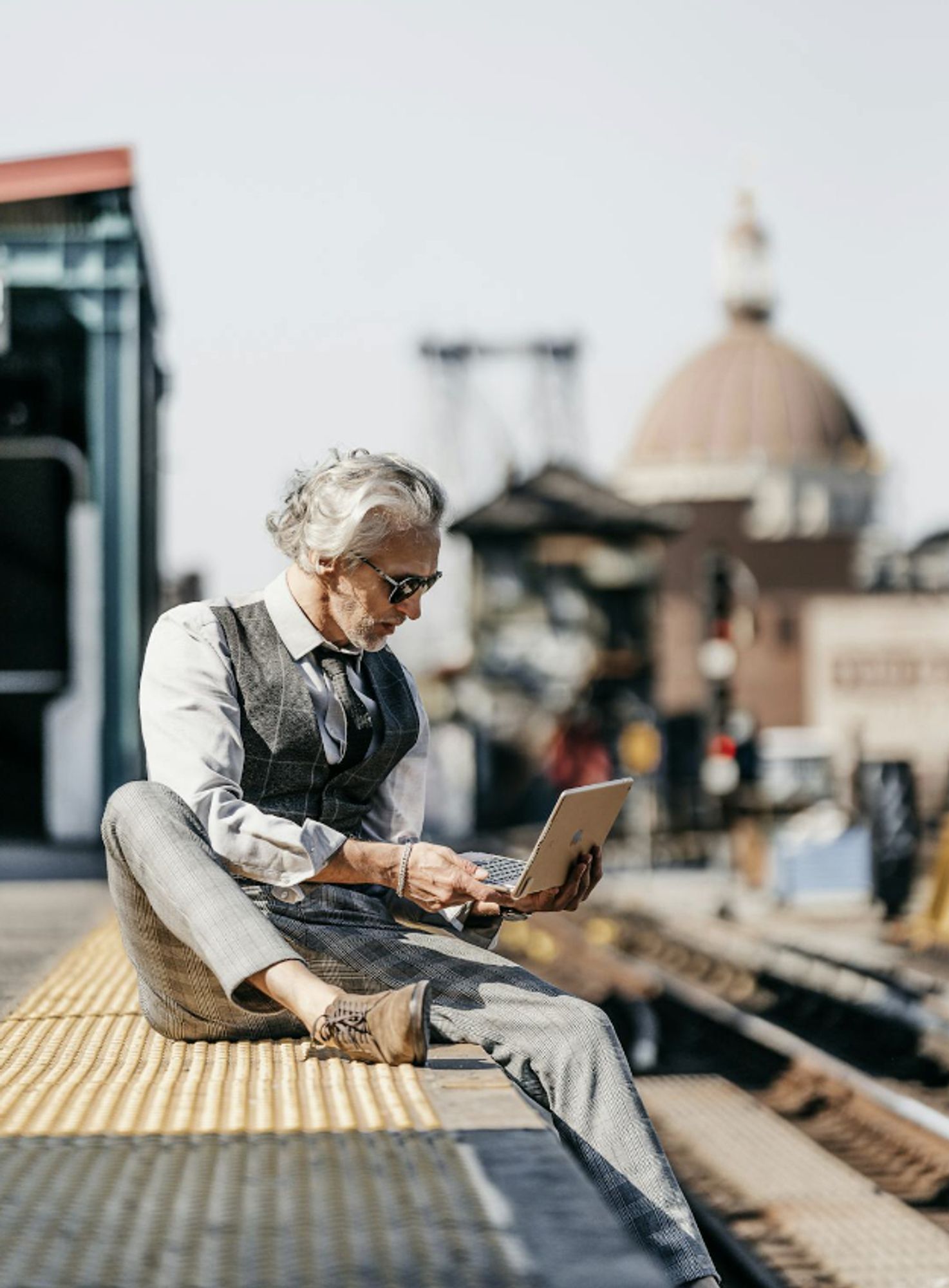 Image of man in suit but without socks sitting on roof with laptop; dome on skyline in background, by Andras Stefuca