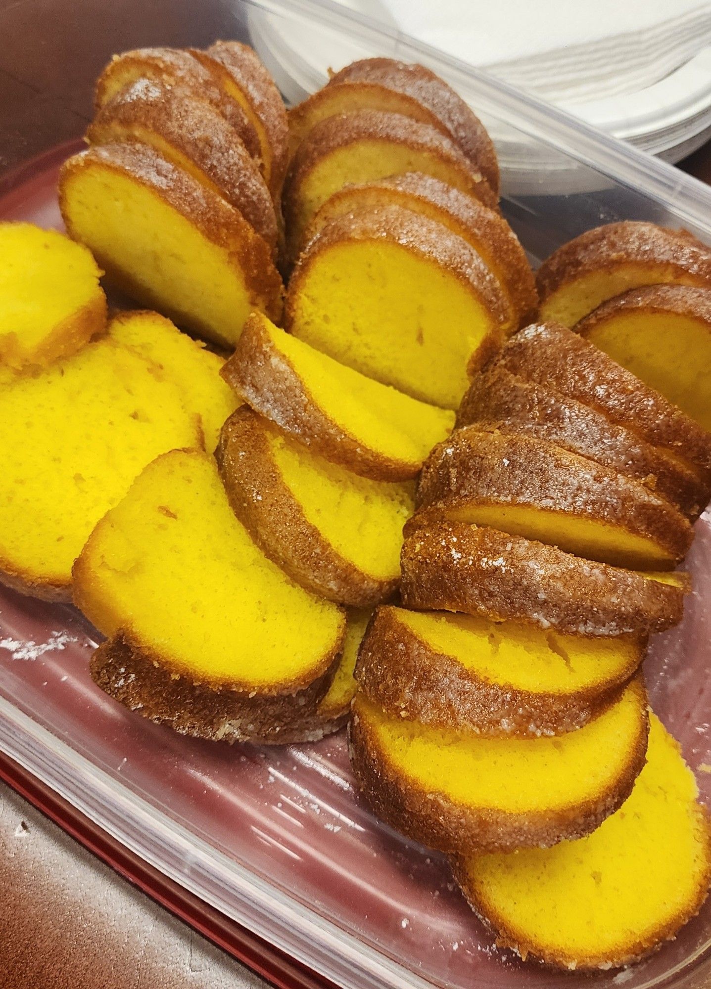 A lemon cake sliced up in a Tupperware. It is very yellow and delicious looking. 