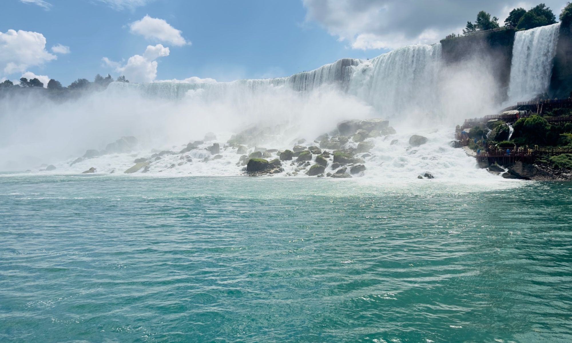 Niagara Falls on a perfect sunny day with a few clouds. Niagara River is pouring over the US side in misty white waves, terminating on the rocks below, and moving on into blue calm waters.