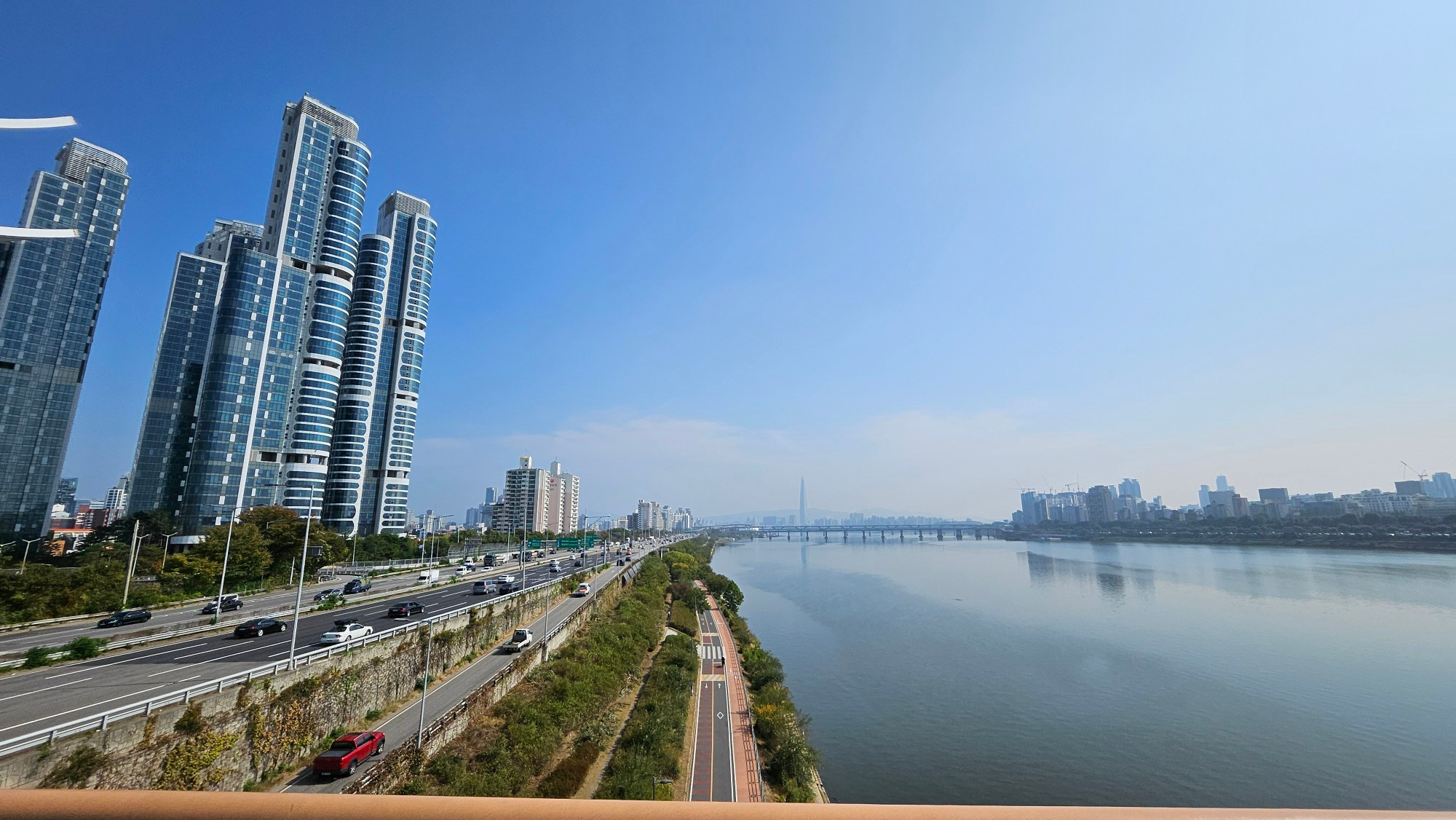 Han River from a high vantage point, with skyscrapers to the left and off in the distance with the roadway with traffic underneath 