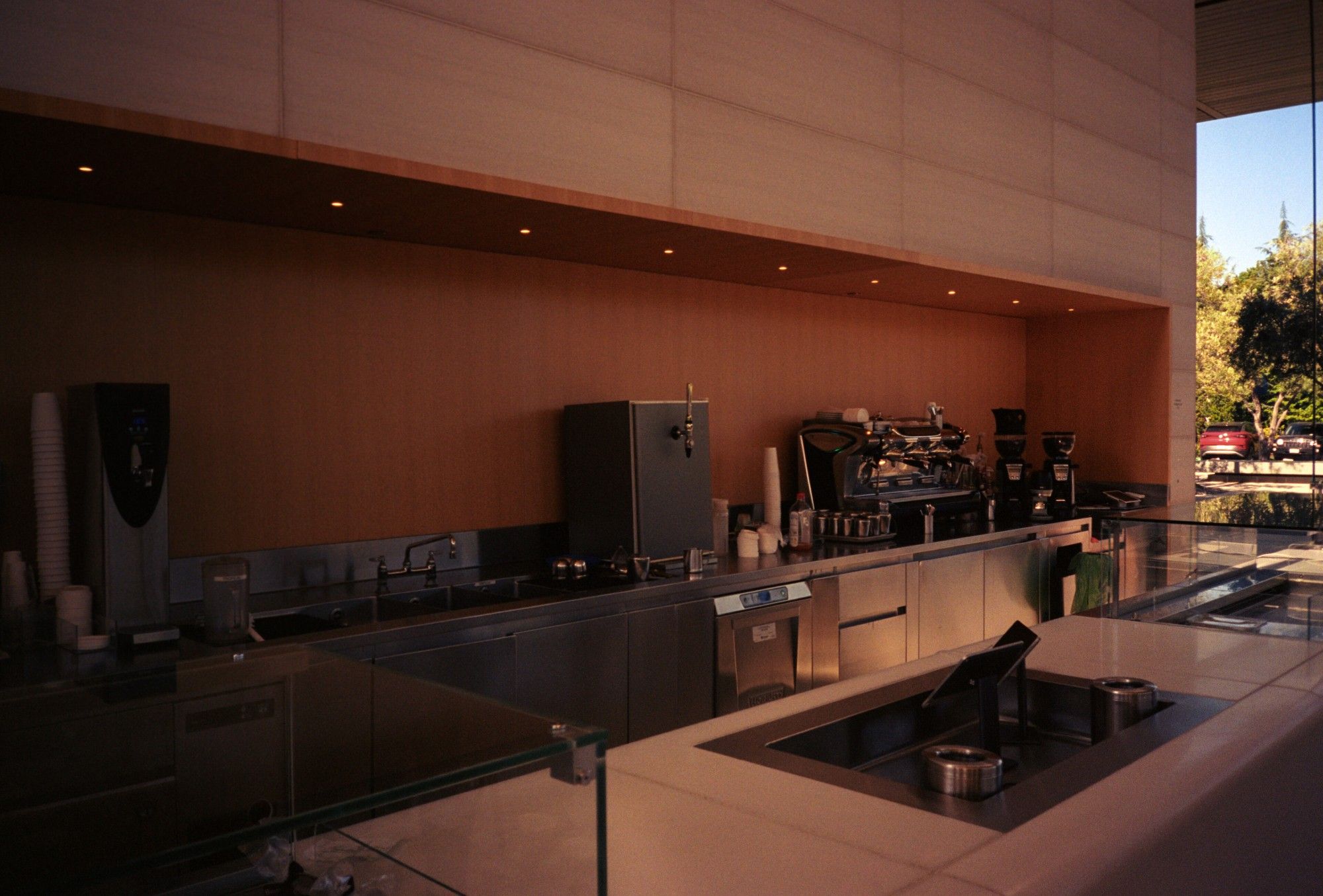 A photo of the cafe at the Apple Visitor Center. In the foreground is the sales counter, back behind it, is the preparation counter. The prep counter is recessed into a cove in the wall lined with brown a darker brown wood than the surrounding wall.