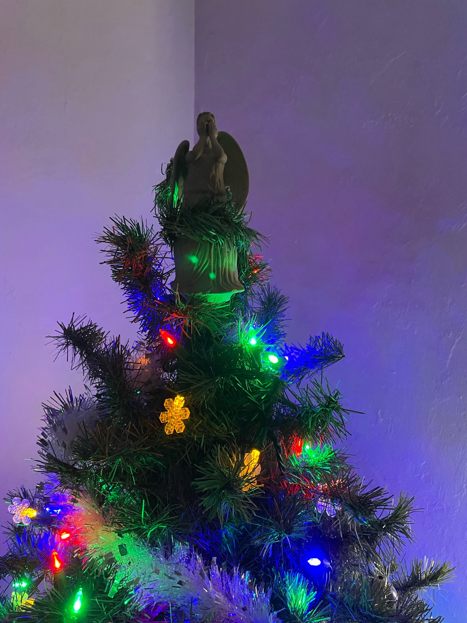 Our tree this year: a fake green fir, strung with bright lights in blue, red, and green and yellow snowflake lights. I don’t know why they came in yellow. They’re white on the package. Anyway, best for last, star of the show, is a rubber squeeze toy of a Weeping Angel from Doctor Who. She’s got some tree wrapped around her to keep her there. Hope it works!