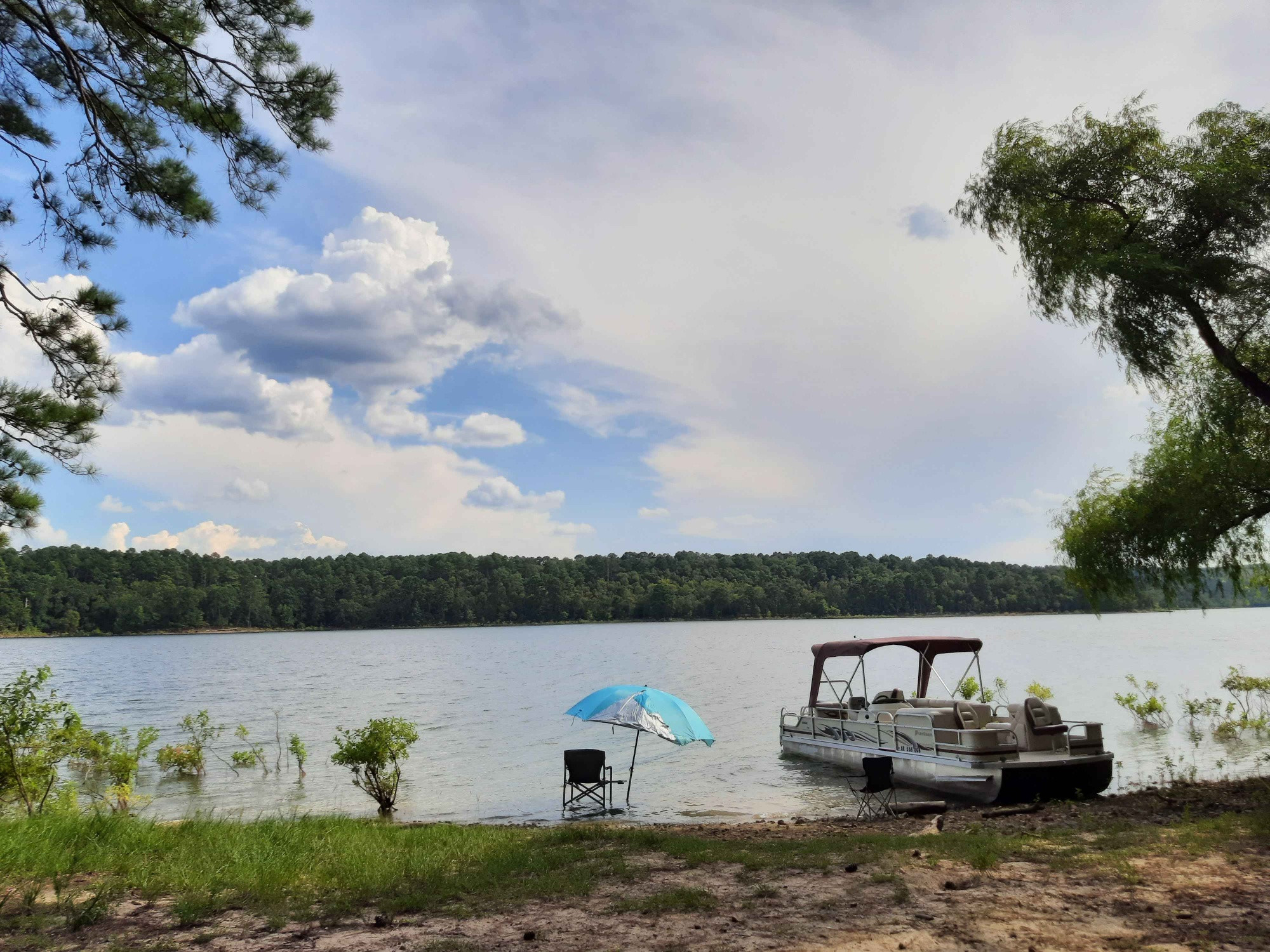 Overlooking a local lake in my state. On the shoreline is a camping chair with an umbrella over it and a docked boat.