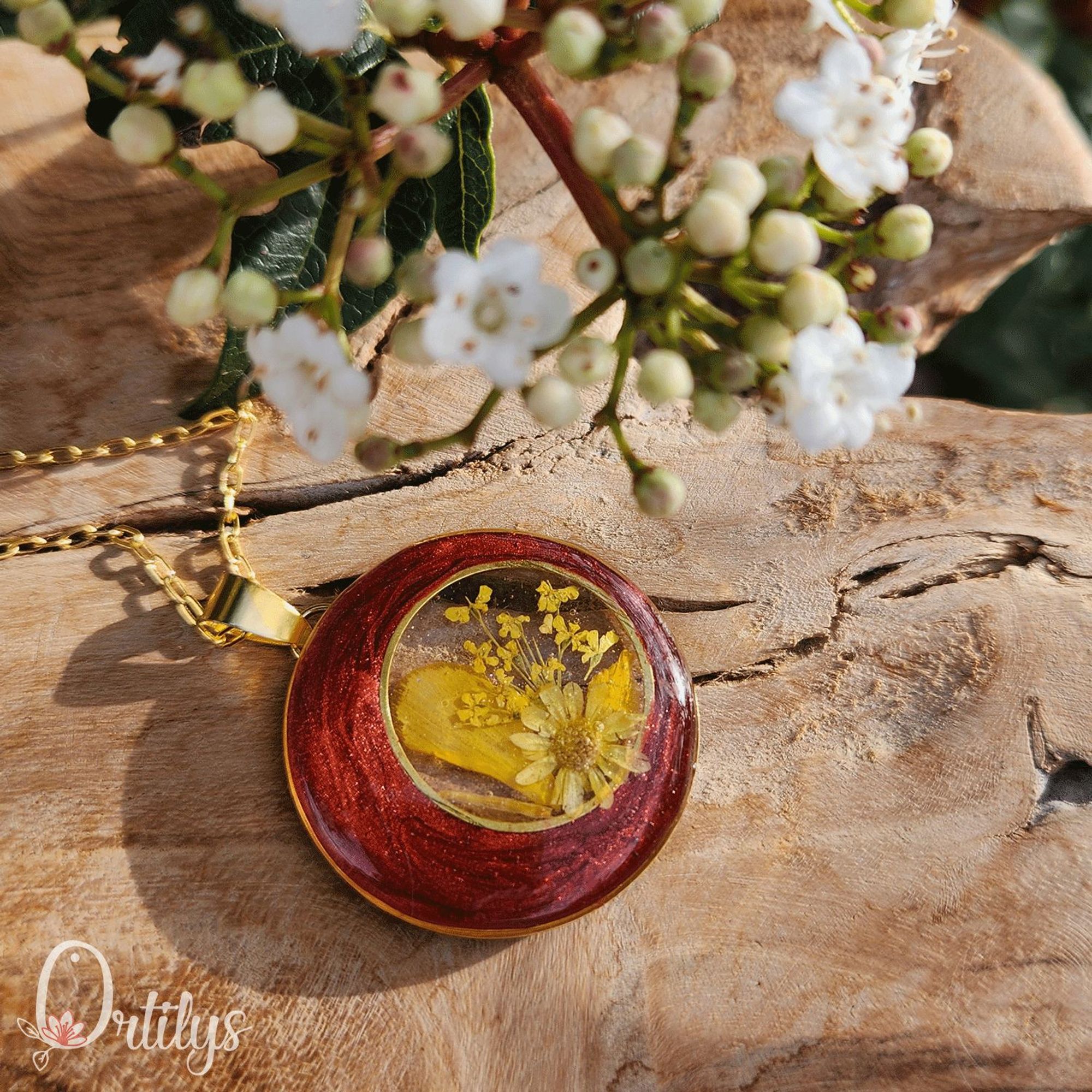 Un collier doré, dont le médaillon est de forme ronde. Un contour en forme de lune, de couleur cuivré, le centre est transparent et laisse la part belle à des fleurs et pétales jaunes