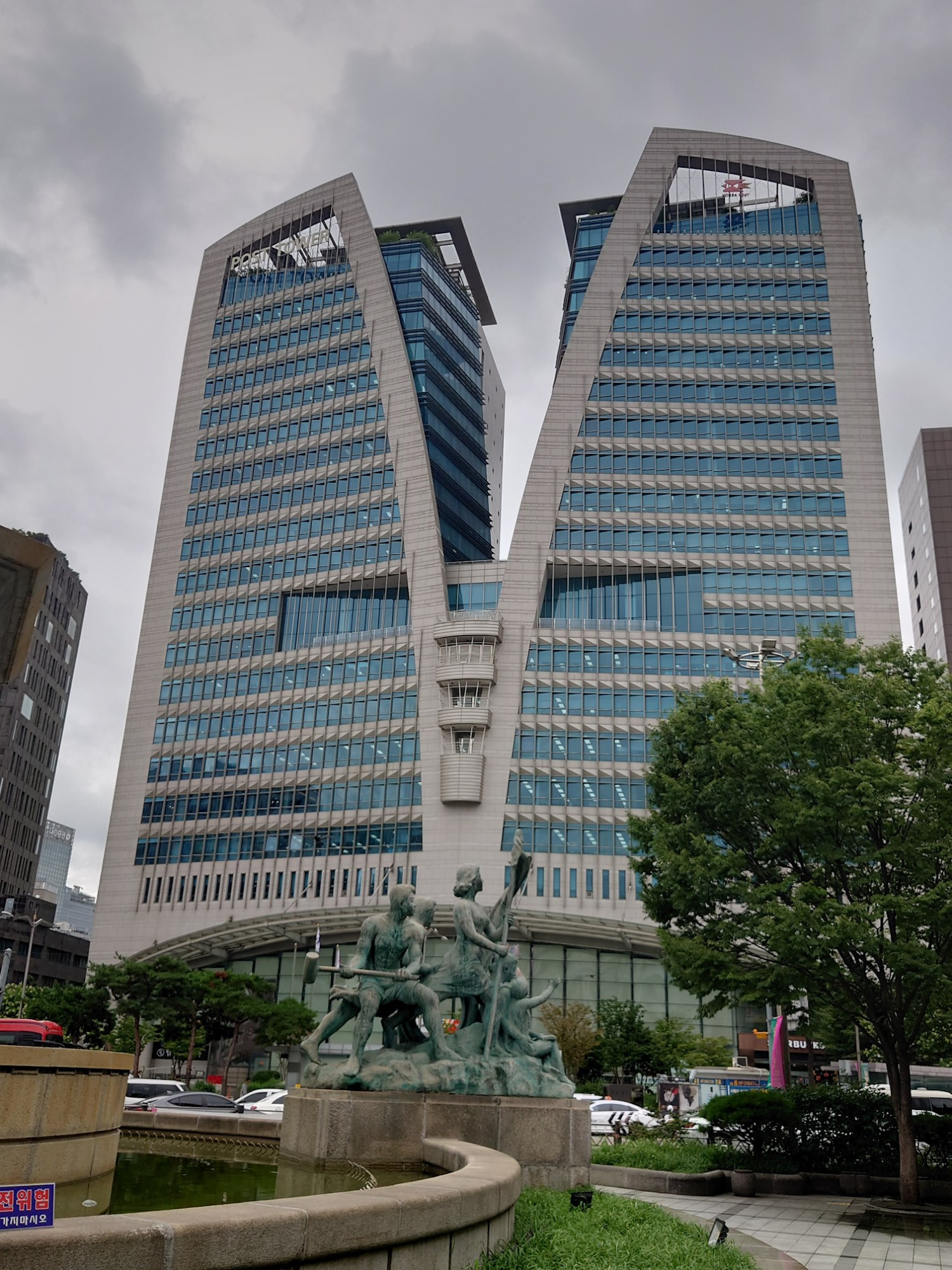 La Korea Post Tower à Séoul. Au premier plan, un des groupes de la fontaine de la Banque de Corée, le 23 juillet 2024.