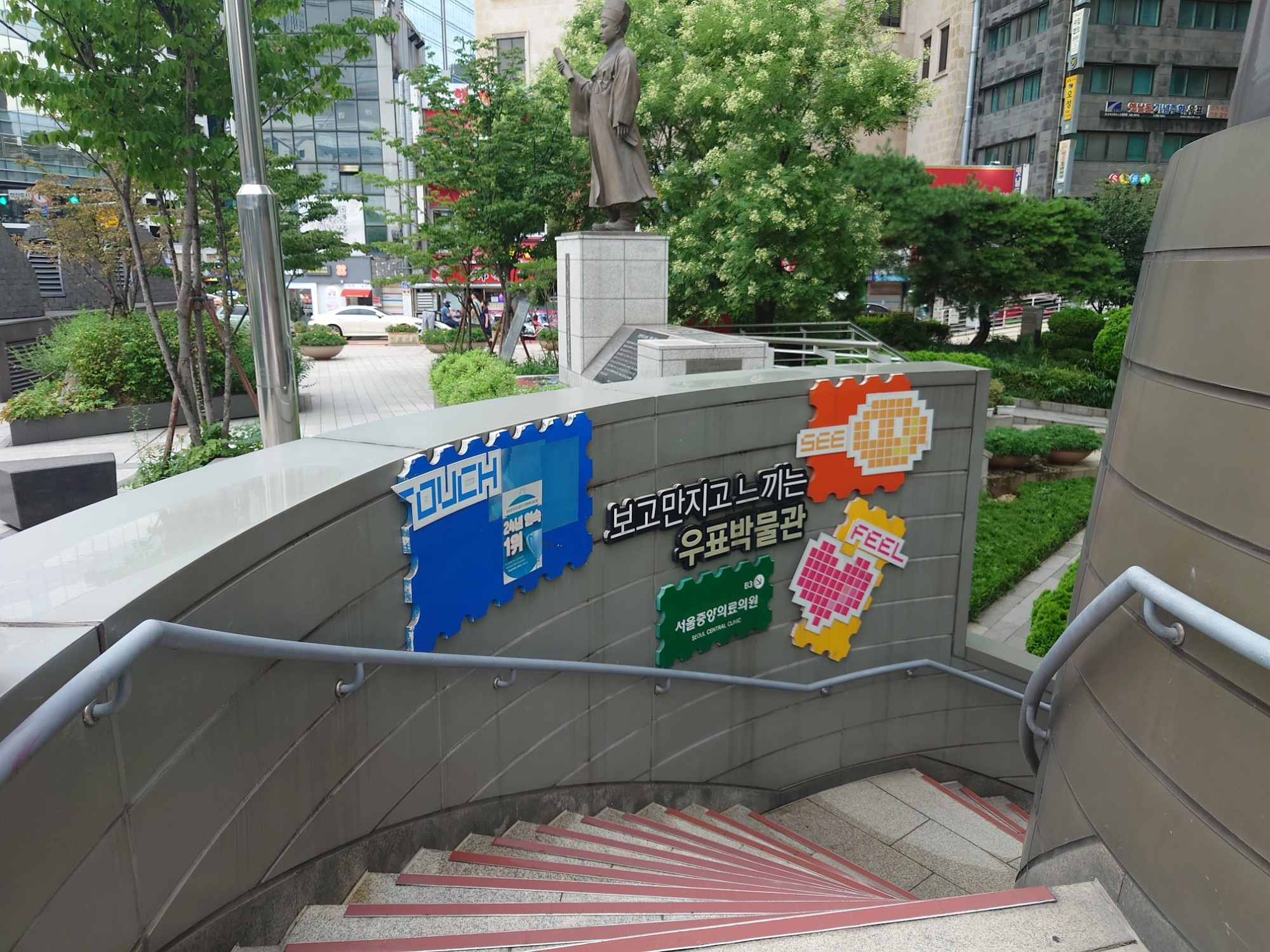 À gauche de la boîte aux lettres, l'escalier vers le bureau de poste et le musée des timbres-postes au premier sous-sol de la Korea Post Tower, le 23 juillet 2024. Les dessins attirent sur les activités manuelles du musée ; couleurs et dessins enfantins marquent beaucoup l'espace coréen.