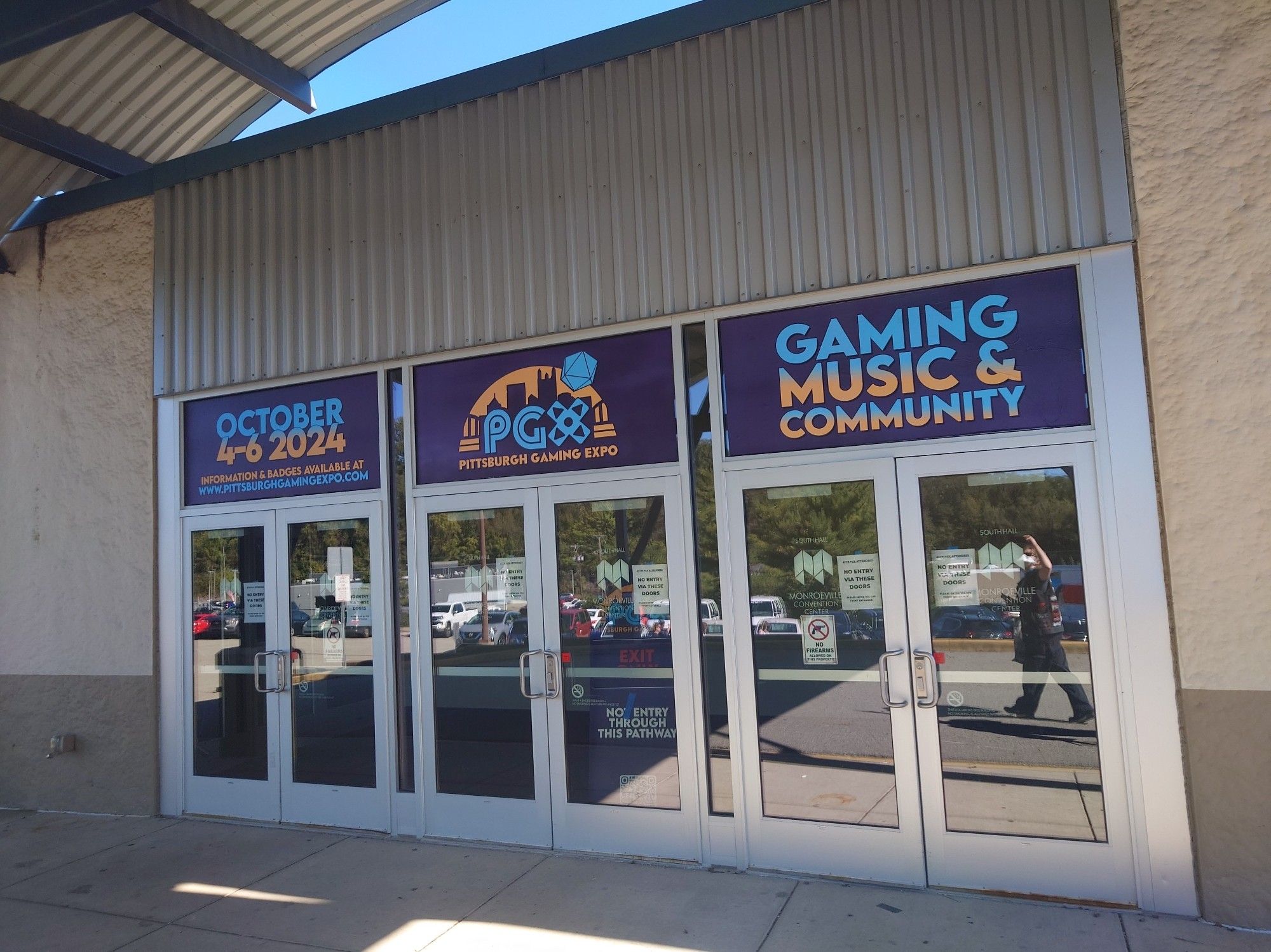 The outside of the Monroeville Convention Center with three signs advertising the Pittsburgh Gaming Expo. The left one says "October 4-6 2024," the center one says "PGX," and the left one says "Gaming Music & Community."