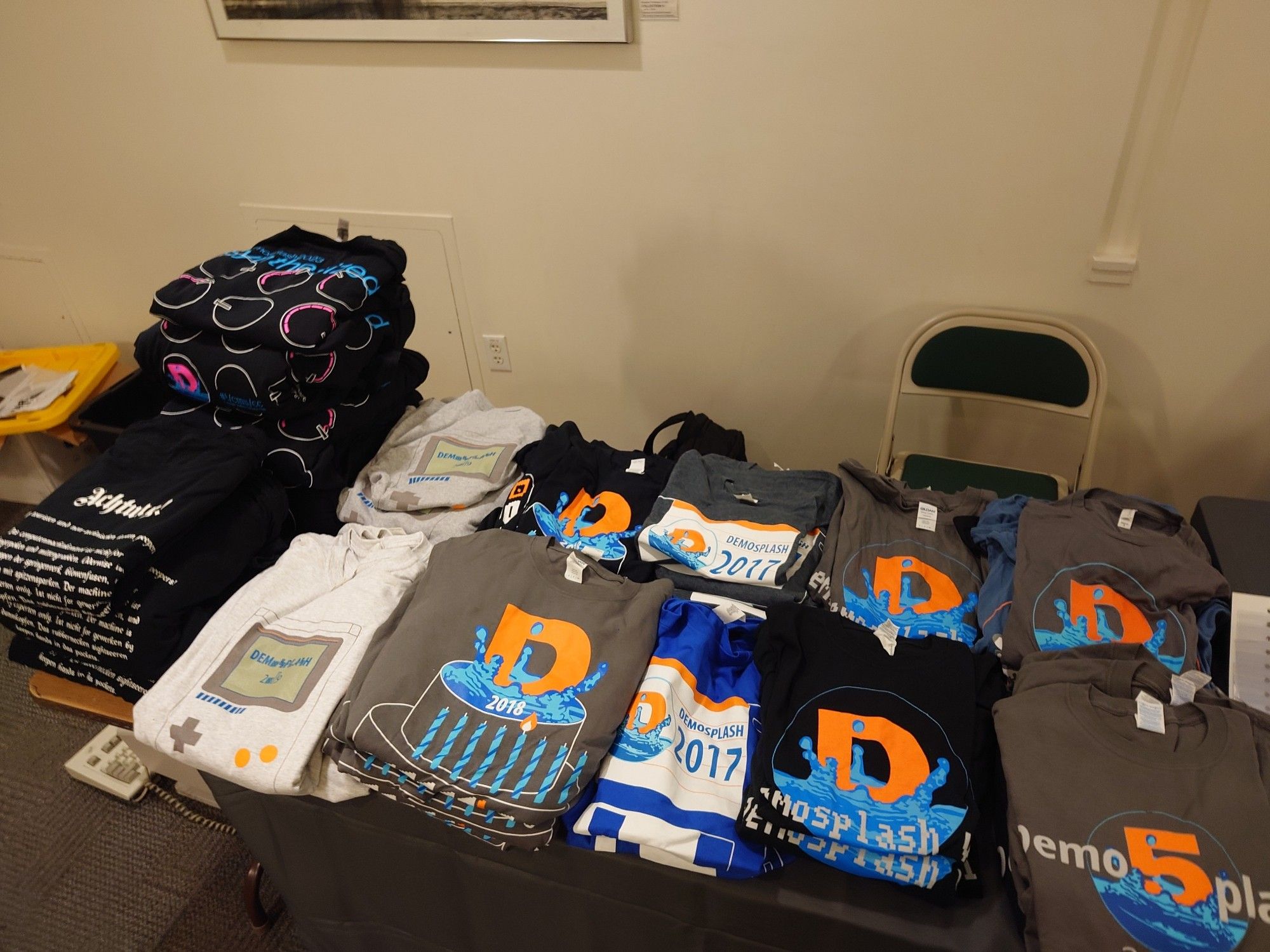 Rows of Demosplash shirts folded and displayed on a table for sale