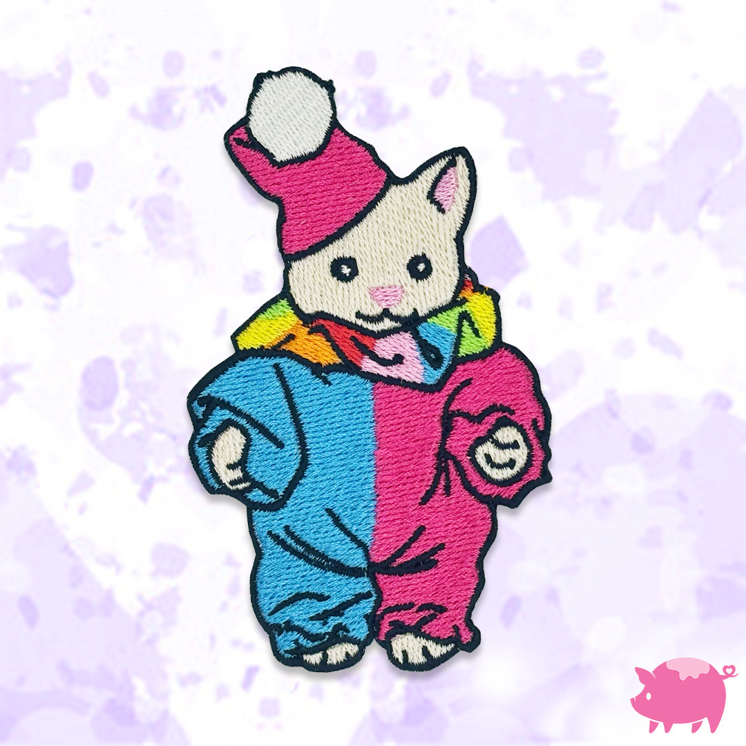 A cream cat wearing a multicoloured clown outfit.