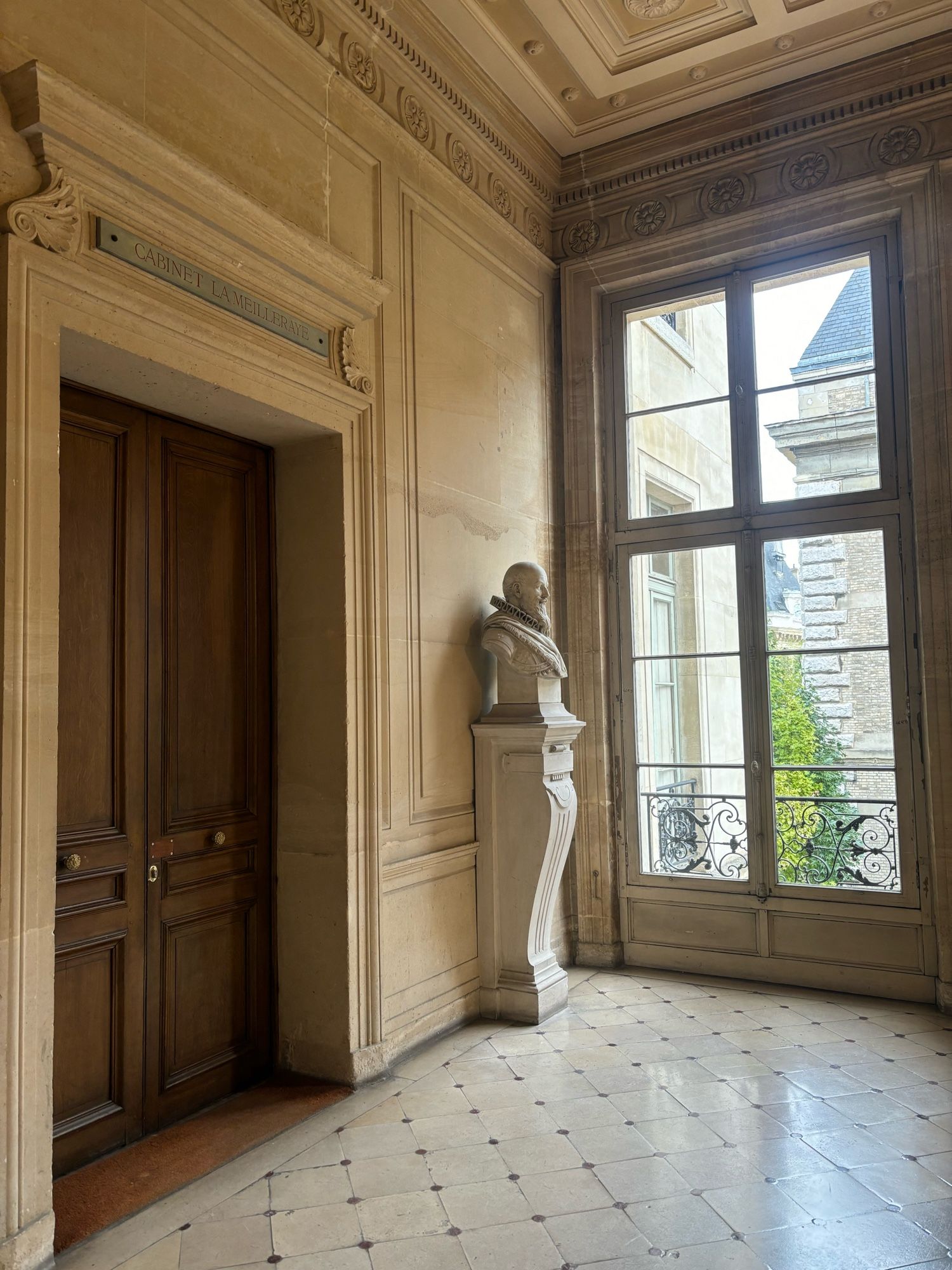 Oak door photographed sideways, to show stone walls, losange floor, a bust statue and a tall window opening on yet more architecture angles and details - all very 17 and 18th century