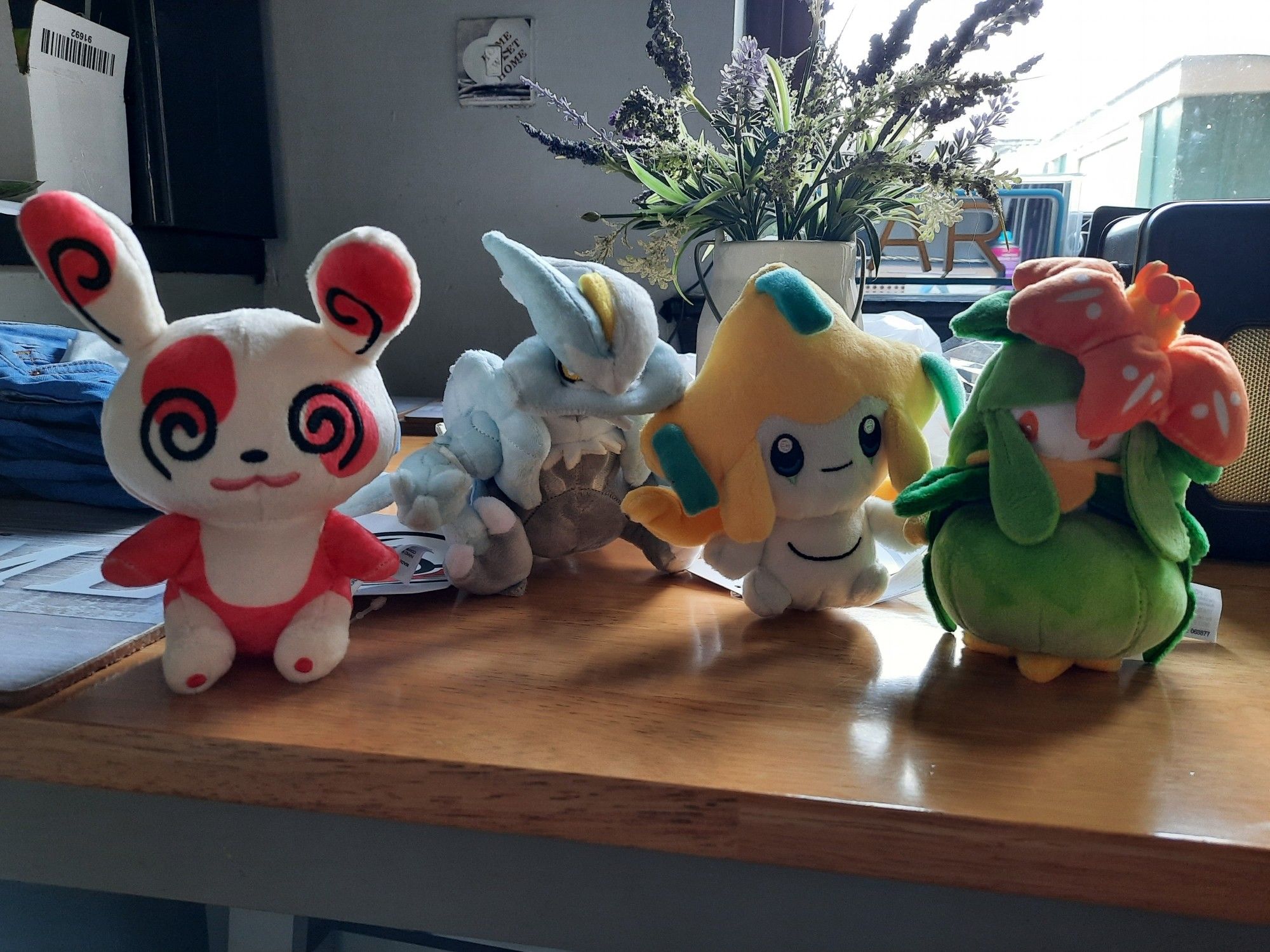 Plush toys sat on a table. From left to right: Spinda, Kyurem-White, Jirachi and Lilligant.