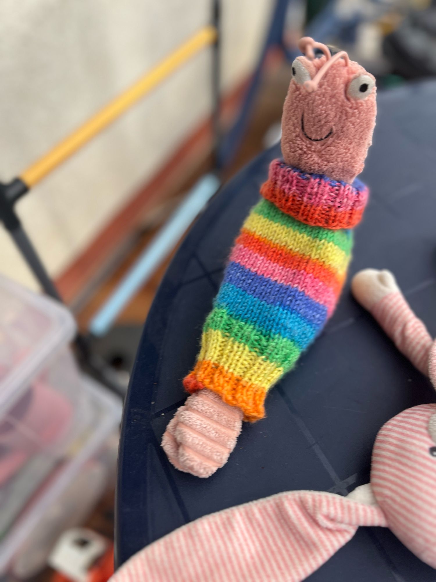 Sheldon, der jellycat schrimp, in seinem gestrickten Regenbogenpullover mit Rollkragen.