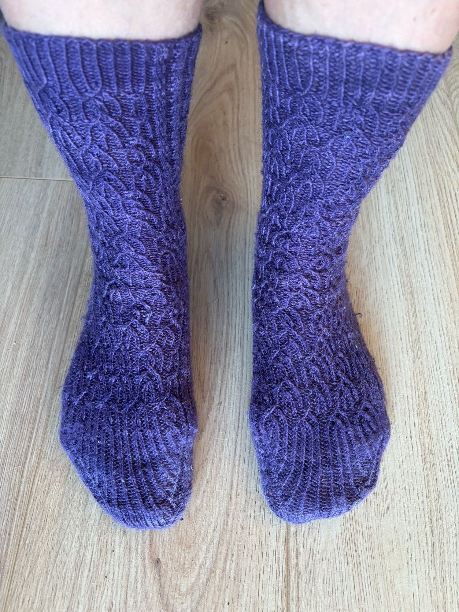 a pair of purple wool socks with an intricate pattern, being worn by a white human of whom you can only see a small amount of leg 