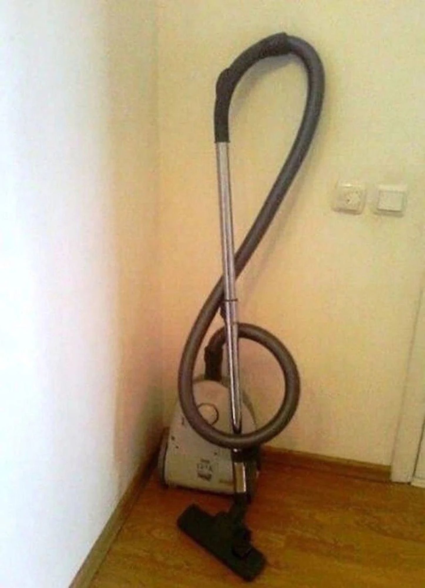 Aspirateur dont le tuyau et le manche tubulaire forment une clef de sol.