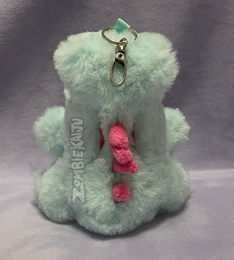 same plush photographed from the back.  the pink spikes and pink embroidered stripes on the back can be seen, as well as the keychain attachment sewn into his head