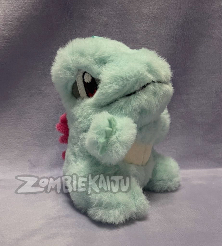 handmade plush of the Pokèmon Totodile, a blue/teal crocodile.  It is made with a short but extra fuzzy fur for the blue parts, a shorter minky fabric for the other details, and felt claws sewn into his hands.  his eyes and mouth are embroidered on