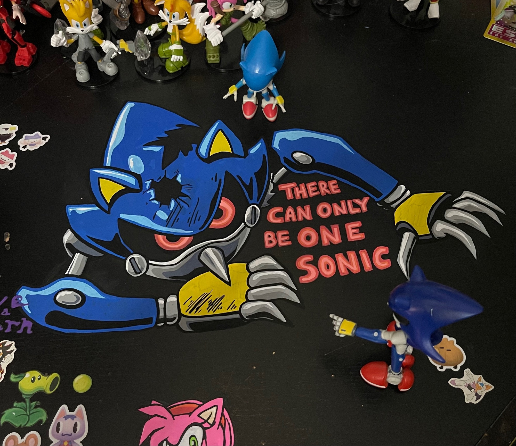 doodle of Metal Sonic from the Sonic CD OVA, done in posca pens on a black desk.  The text “THERE CAN ONLY BE ONE SONIC” is also drawn with the mural, as a reference to the OVA.  Two figures of Metal Sonic stand looking at the doodle