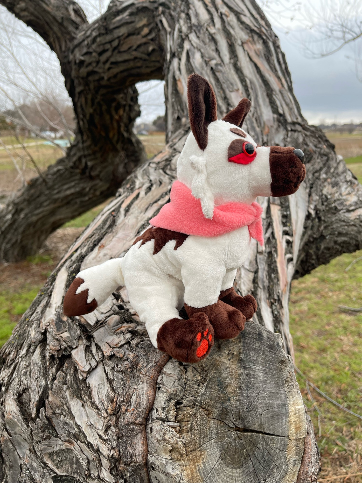 same plush, photographed from the side so that the plush is facing the right side of the screen, still in the sitting pose.  the tail can be seen, cream colored with a brown tip, and brown markings can be seen on it’s back as well