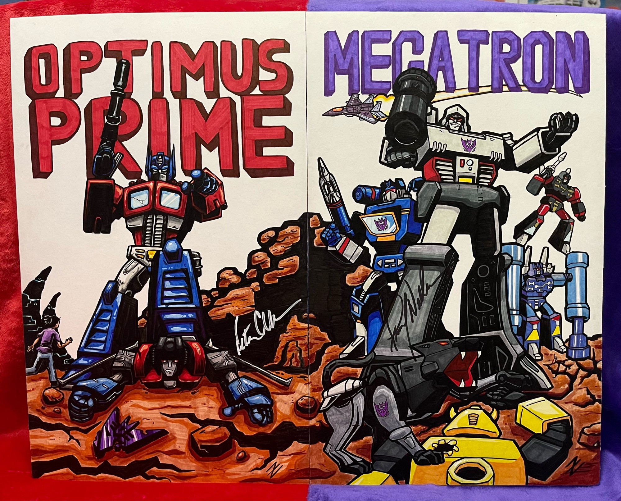 Two ink and marker drawings on large art board next to each other.  The one on the left is of Optimus Prime from Transformers standing on a defeated Starscream, pointing toward the viewer, with a human girl character running toward Optimus (meant to show that he is seen as a safe protector).  The drawing on the right is of Megatron, surrounded by other characters voiced by the same man (Skywarp, Soundwave, Ravage, Rumble, Frenzy), with a defeated Bumblebee on the ground in front of them.  Both drawings are signed by the voice actors of the characters