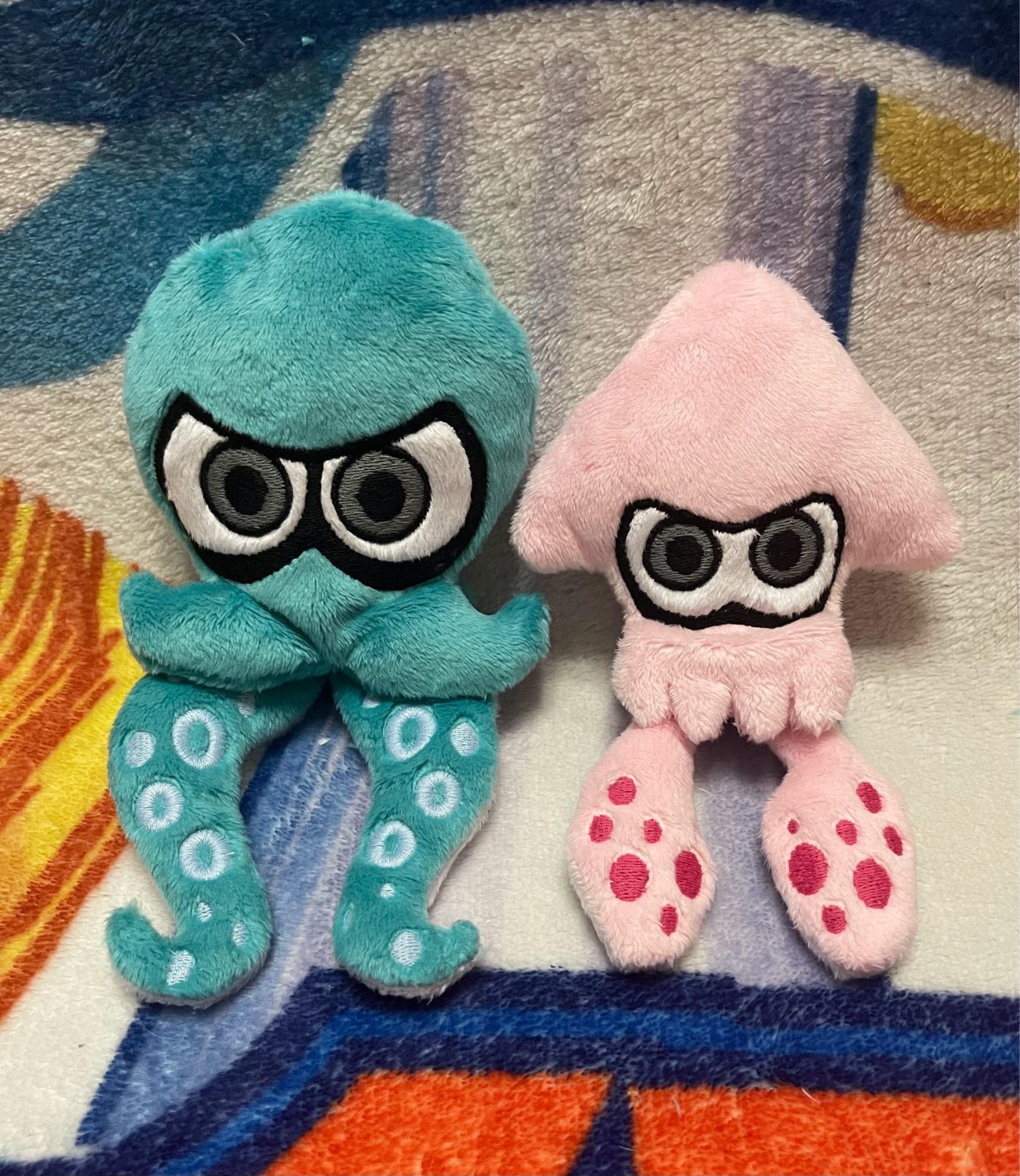 handmade plush of an octopus and a squid from the video game Splatoon.  the octopus is a teal color with light blue spots on its tentacles, with grey eyes.  the squid is a light bubblegum pink color with hot pink spots on it’s tentacles, and grey eyes