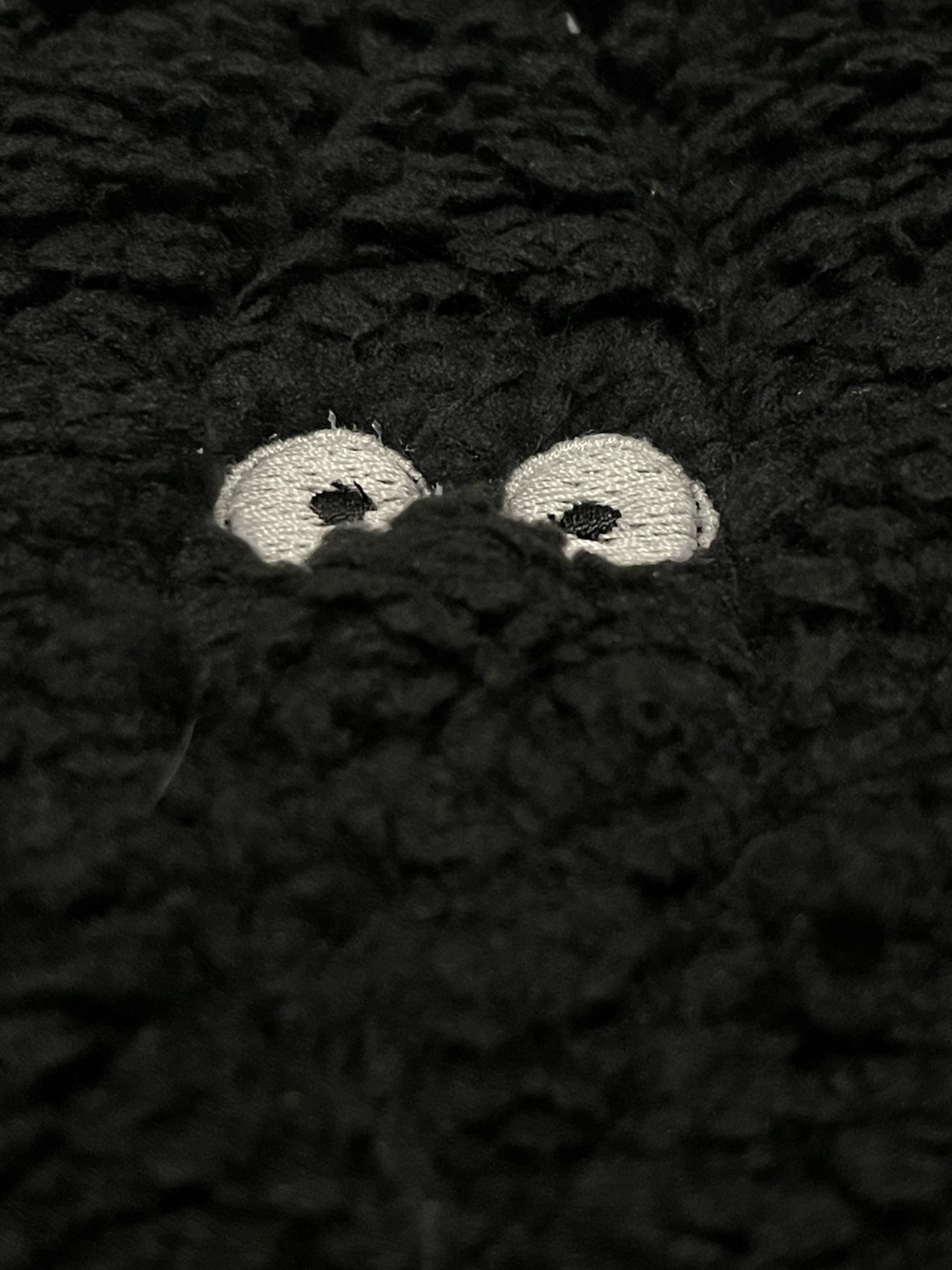 black sherpa fabric with two white circle eyes with tiny black dots for pupils embroidered on