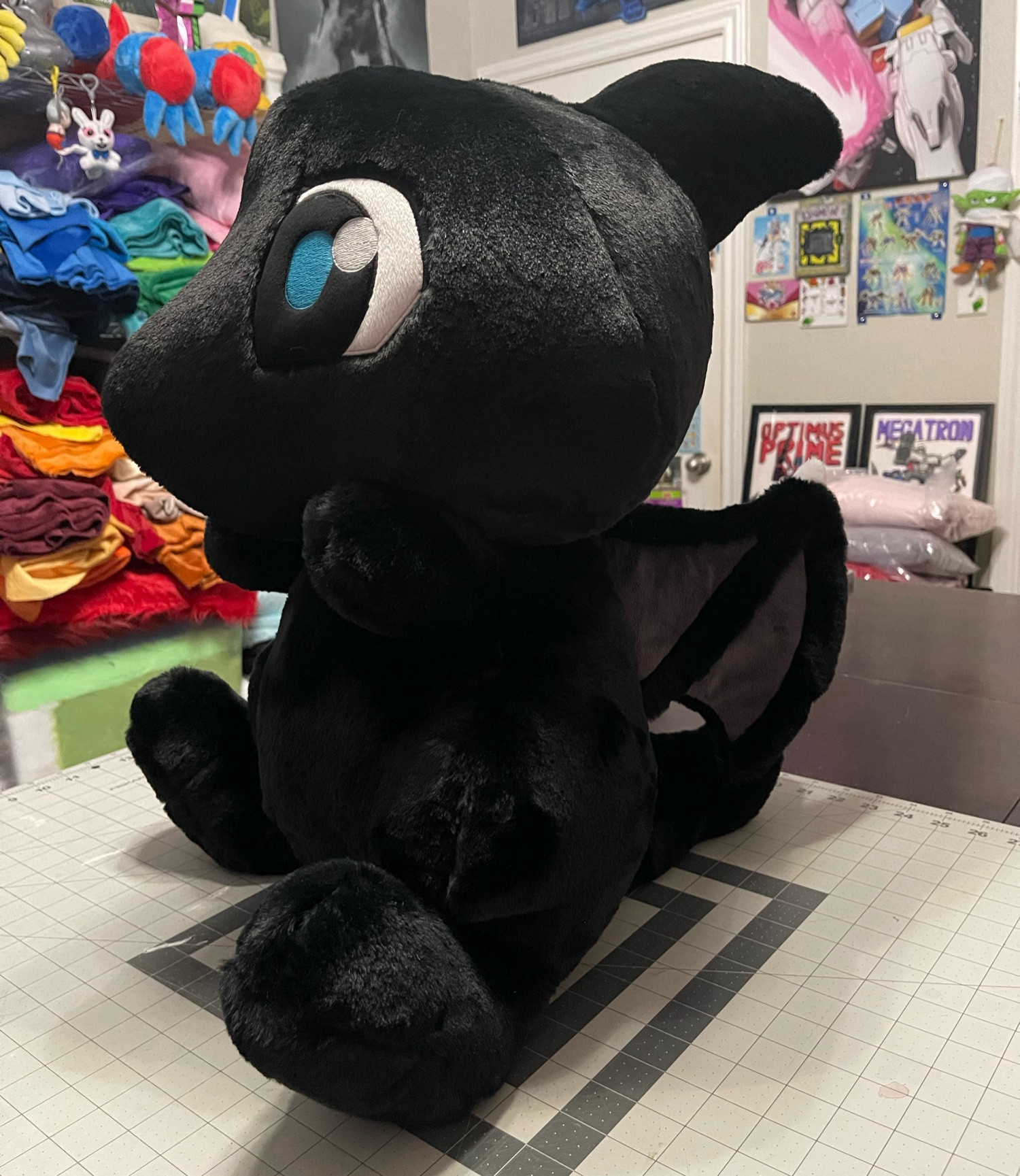 Very big (about 24” tall) handmade plush of a Shadow Shoyru from Neopets, which is a black cartoon dragon with blue eyes and little wings, made with a very fluffy fabric.  The plush is facing to the left