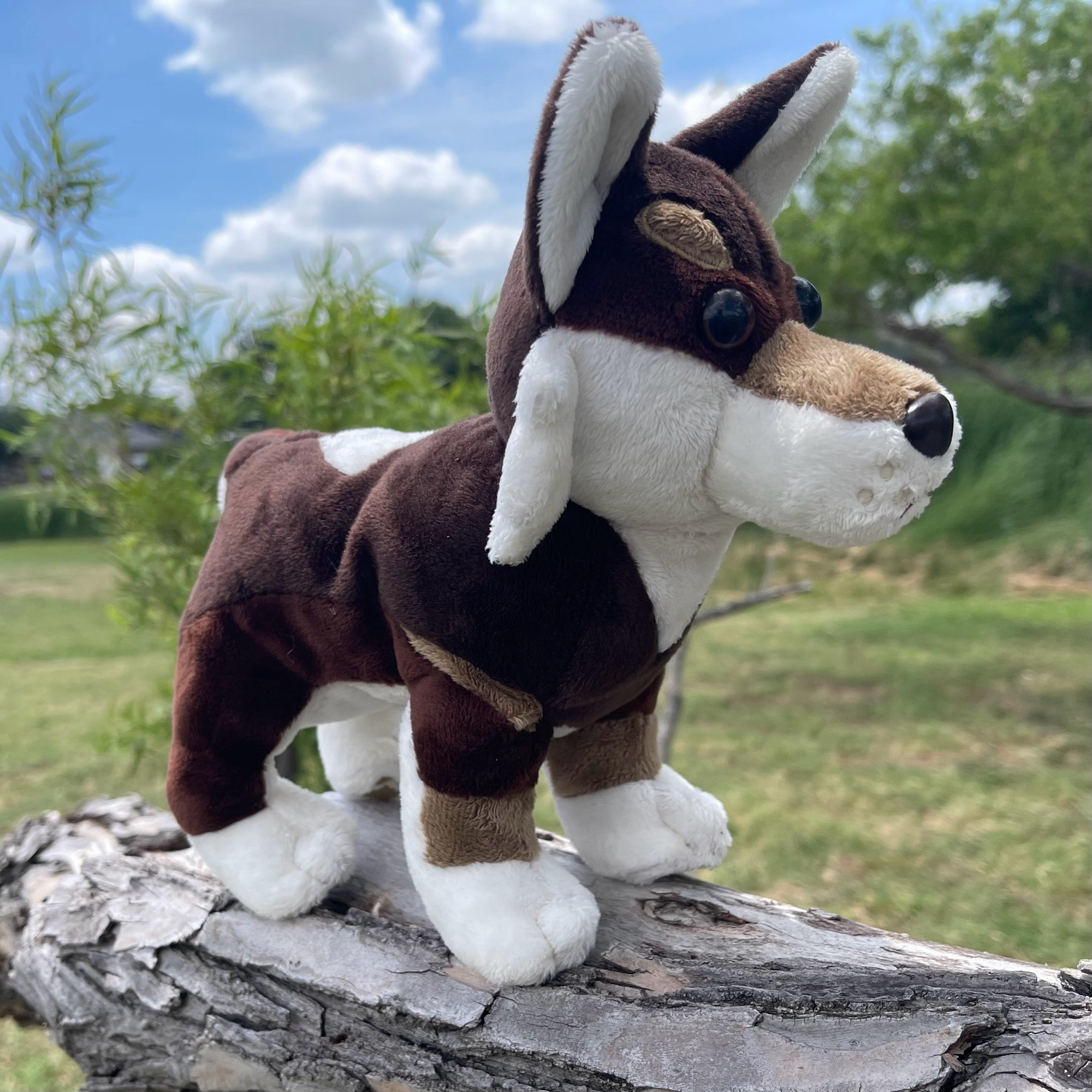 handmade plush of a brown and white wolf standing on a tree branch