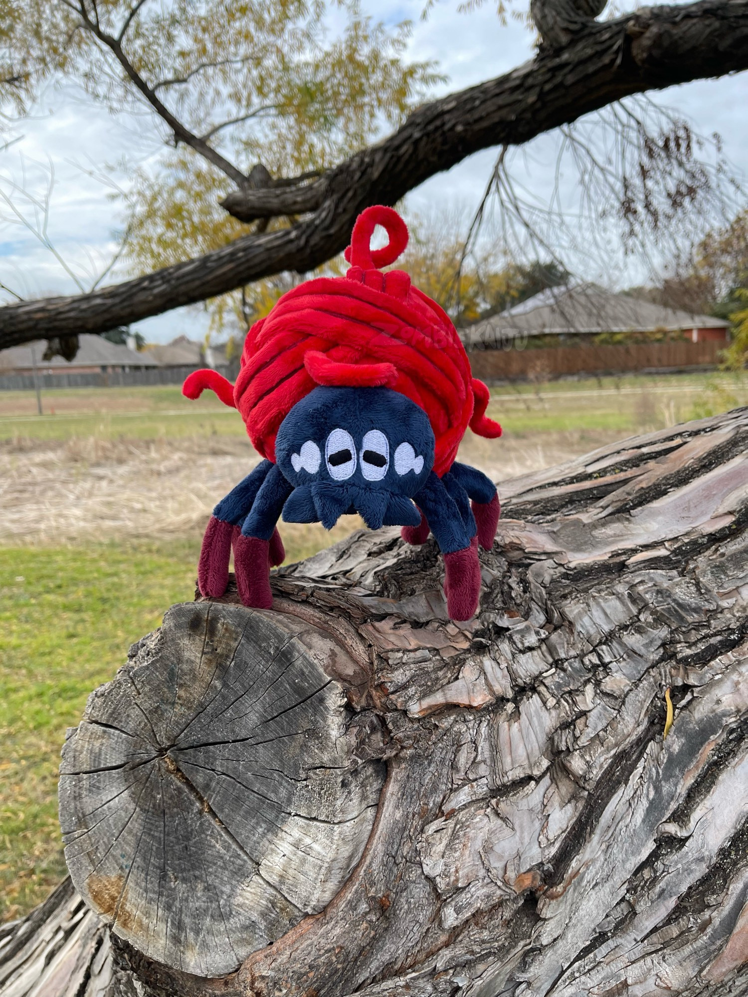 handmade plush of a shiny Tarountula from Pokemon, sitting on a tree.  It is a spider whos body is a red ball of yarn