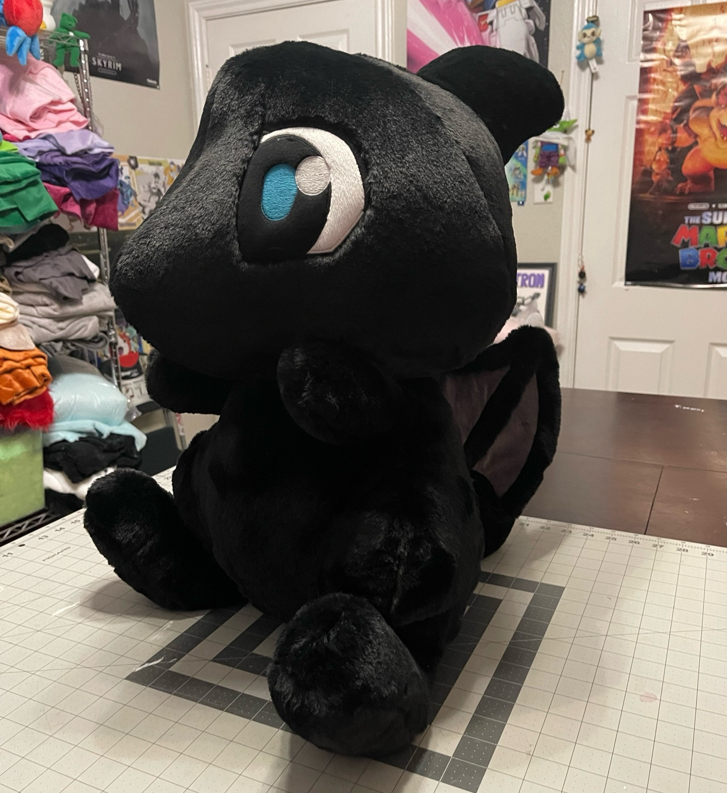 Very big (about 24” tall) handmade plush of a Shadow Shoyru from Neopets, which is a black cartoon dragon with blue eyes and little wings, made with a very fluffy fabric.  Plush is facing the left but angled a bit towards the camera