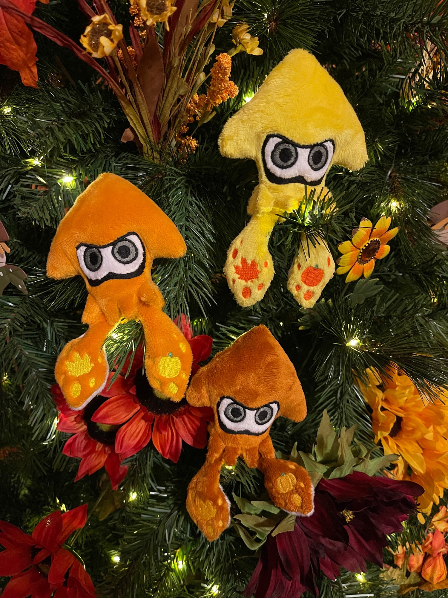 3 different colors (Yellow, Orange, and Rust) of handmade squid plush from splatoon, with embroidery themed around the Fall season, on top of a Fall themed wreath decoration