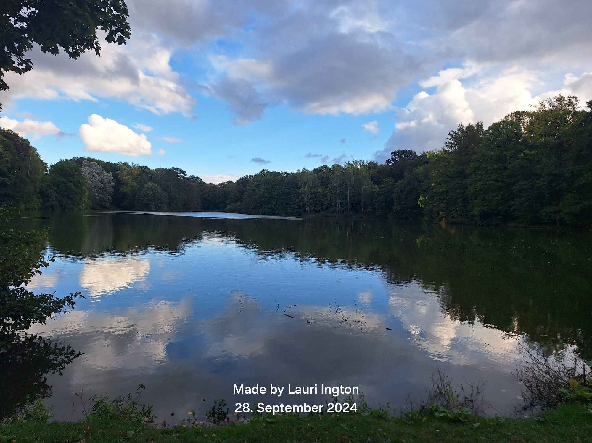 Blick auf den Stadtparkteich mit bewölktem Himmel 
Die Wolken spiegeln sich mit dem Blau des Himmels im Wasser